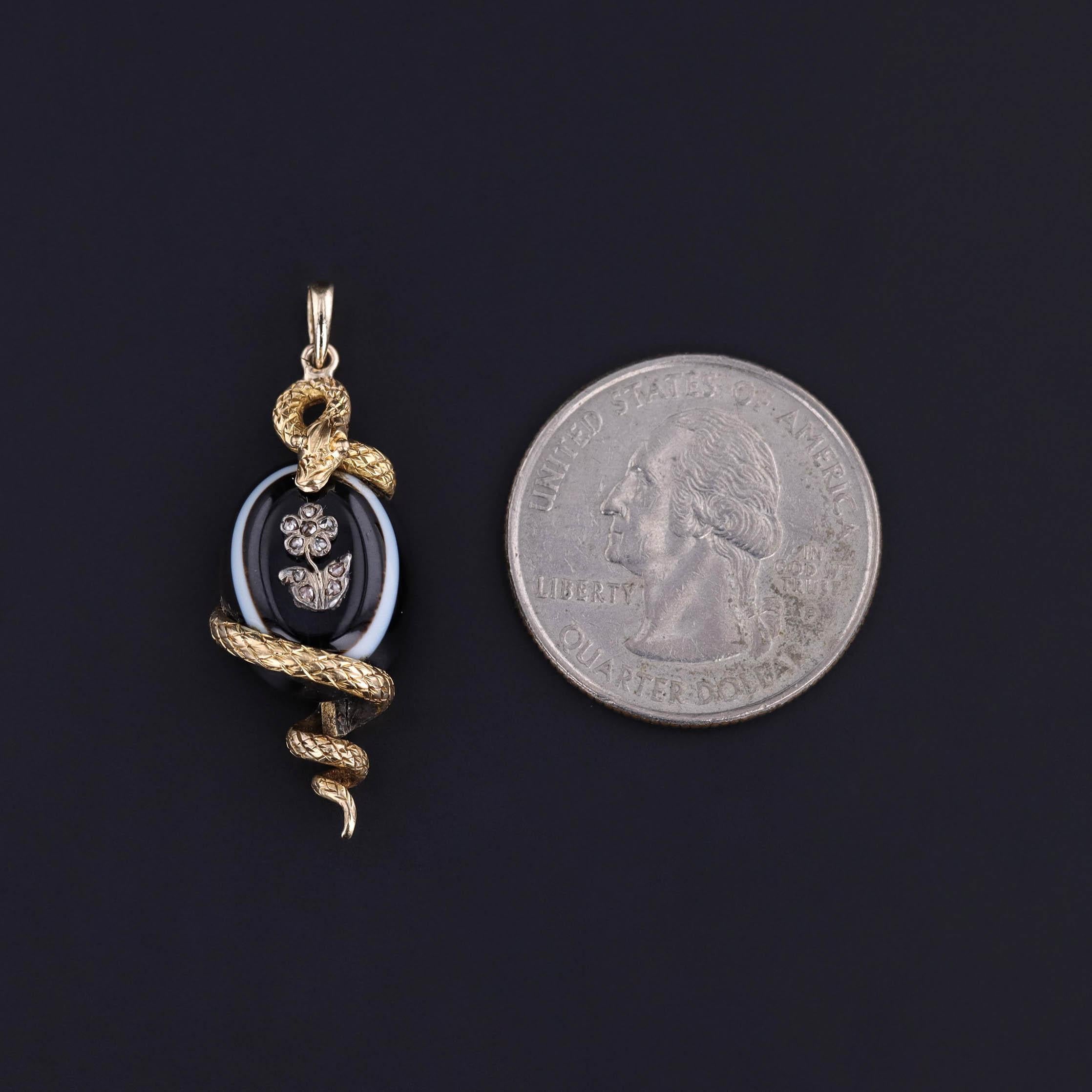 Exemple rare et envoûtant du symbolisme victorien, ce pendentif antique présente un sinueux serpent en or 18 carats enroulé de manière protectrice autour d'une tablette d'agate lustrée, ornée d'une délicate fleur sertie de diamants. Talisman de