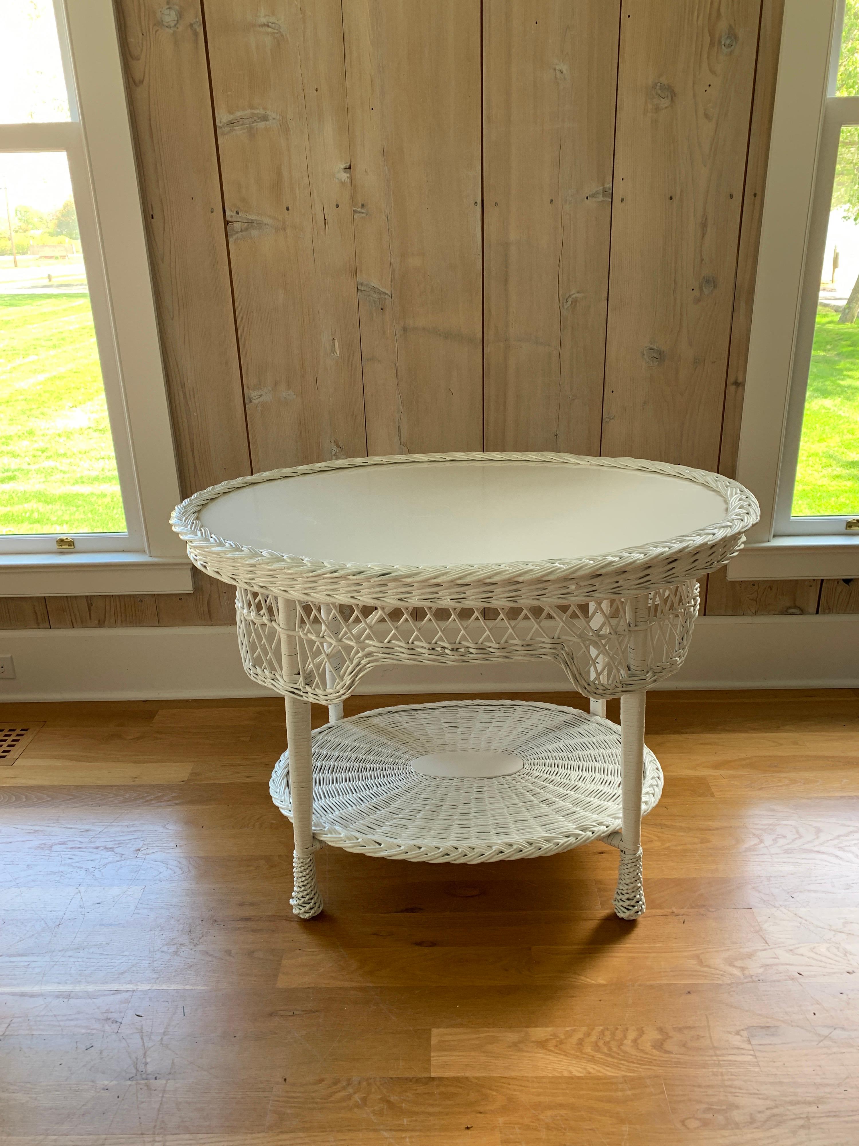 Un tavolo vintage intrecciato in stile Bar Harbor e appena dipinto di bianco. Il ripiano superiore è dotato di un rivestimento a treccia rimovibile che consente di posizionare un tessuto o un vetro sul Wood. Il tavolo misura 39