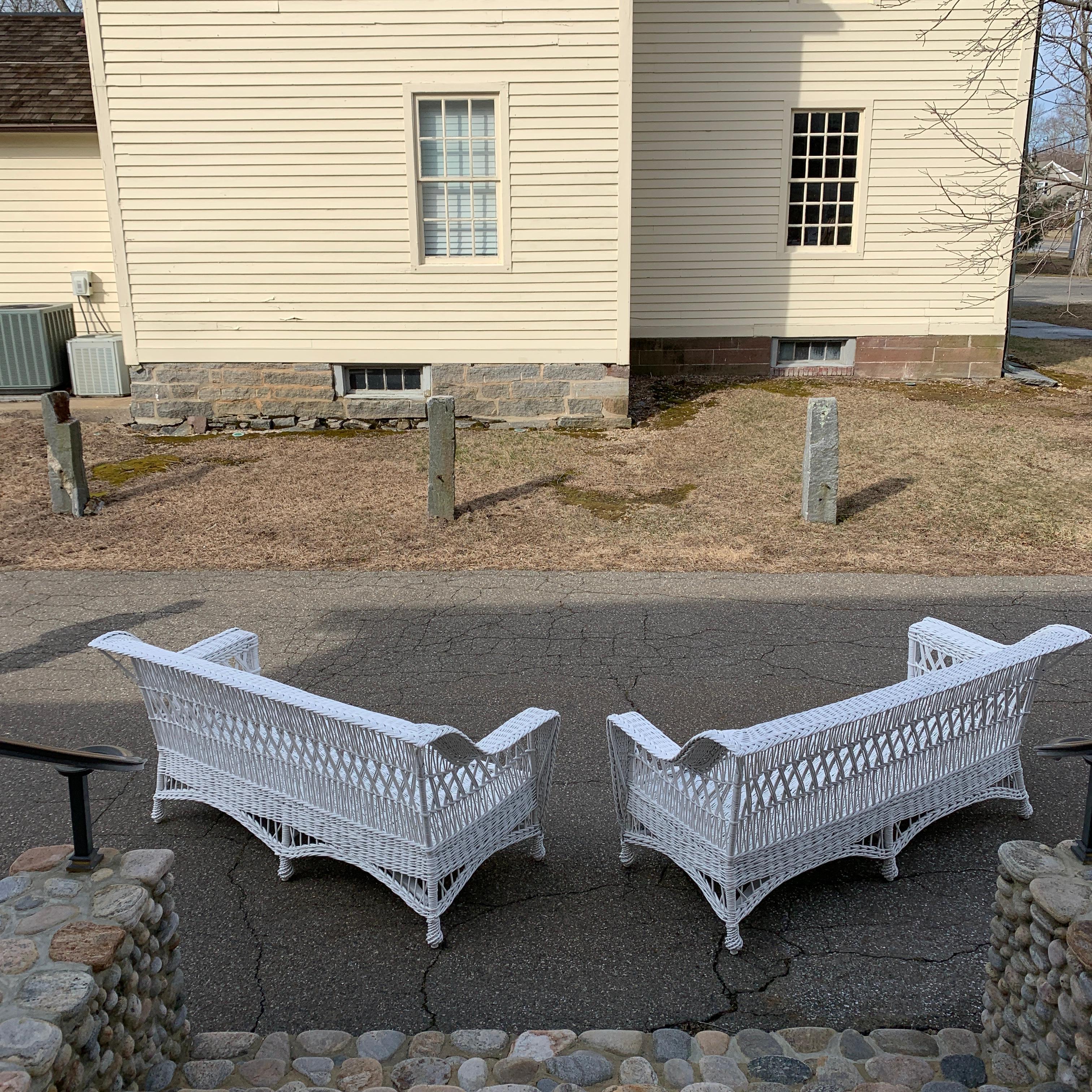 A matched pair of Paine Furniture antique willow sofas in fresh white paint. Intricate pattern woven into the back and sides. Woven seat platform and feet.