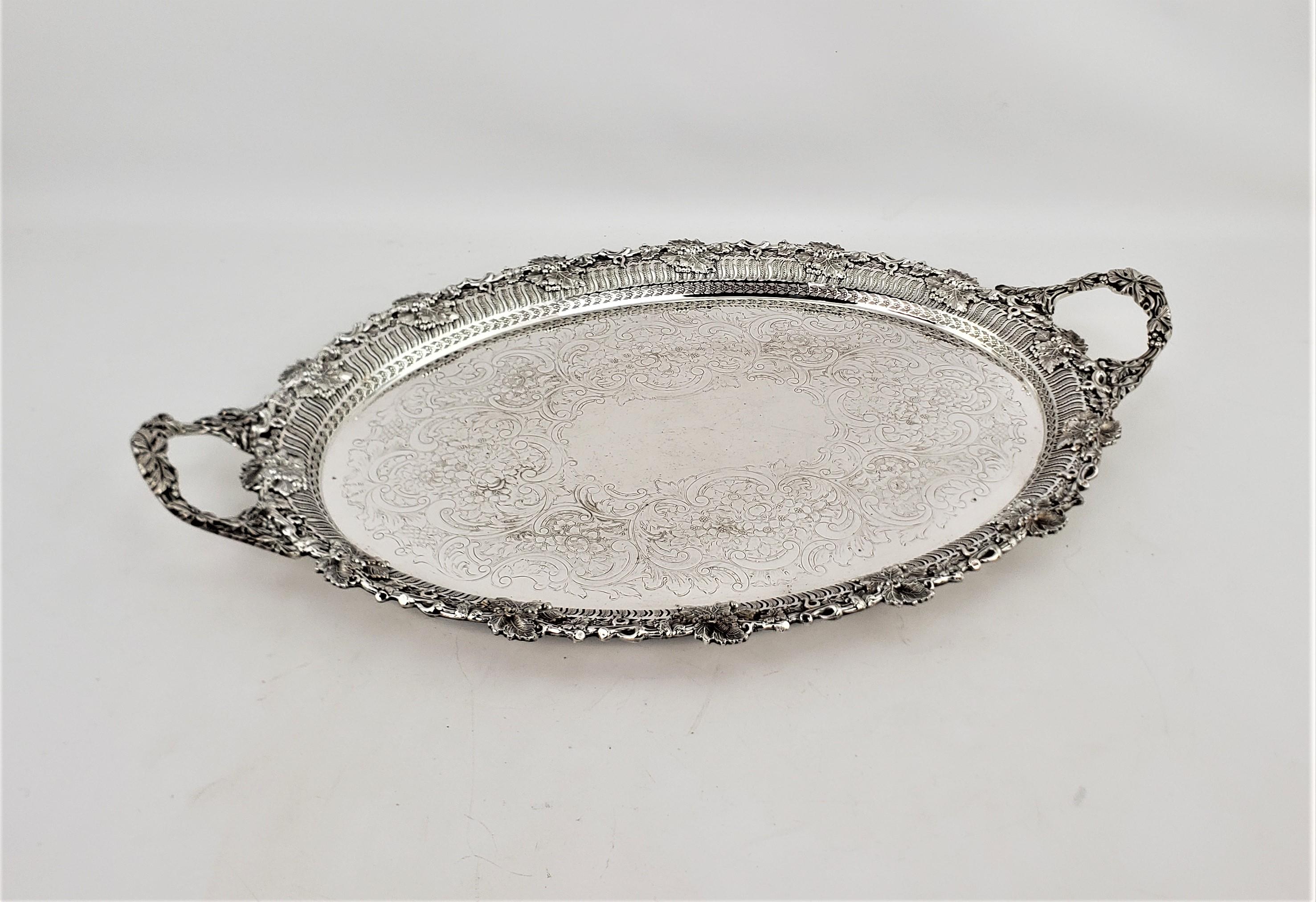 This antique oval footed silver plated serving tray was made by the renowned Barker-Ellis Silver Co. of England in approximately 1920 in a Victorian style. The raised surround of the tray is ornately decorated with oak leaves and acorns, and the