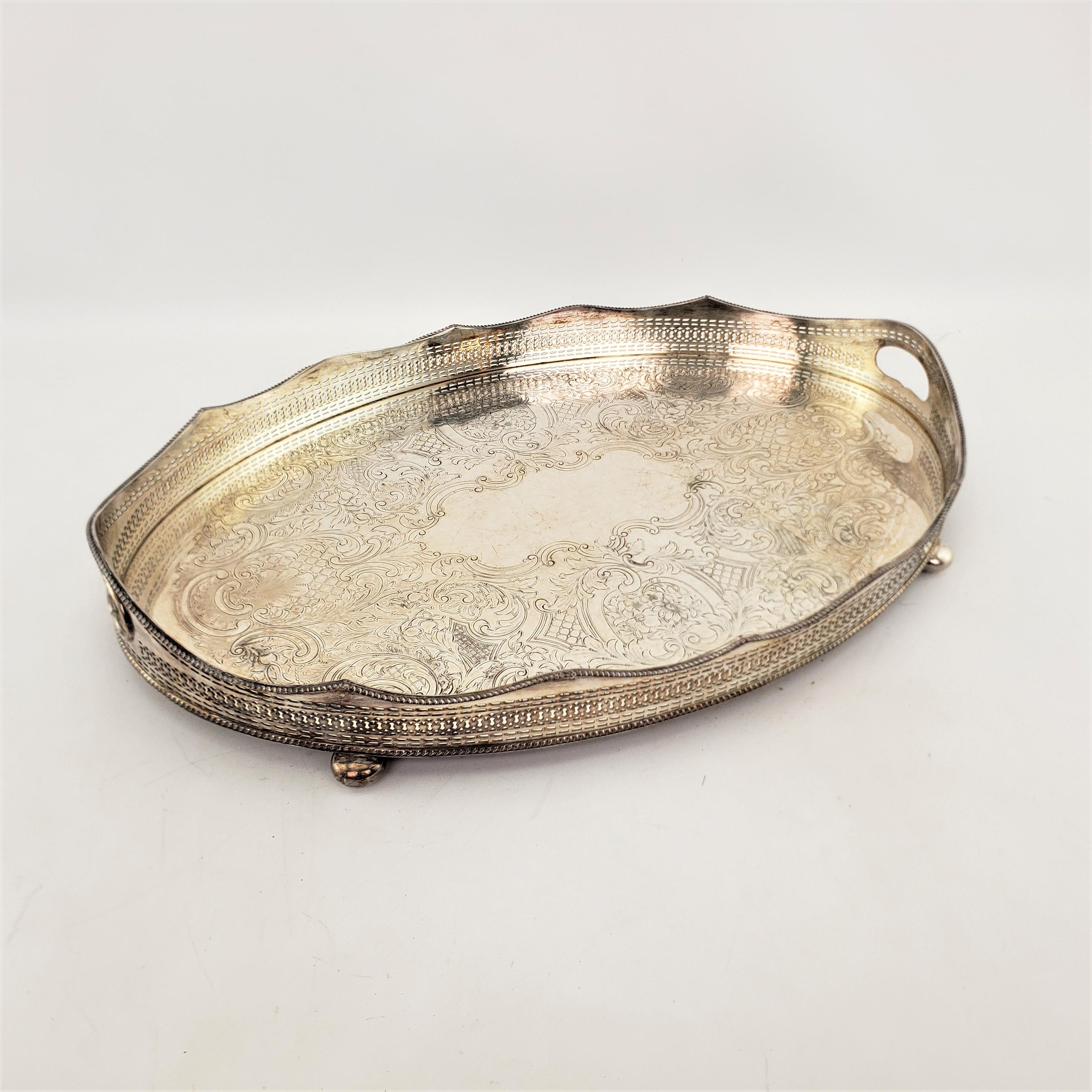 This antique silver plated serving tray was made by the well known Barker-Ellis Silver Co. of England in approximately 1920 in a Victorian style. The tray is composed of silver plate over copper and has a high pierced gallery with inset handles on