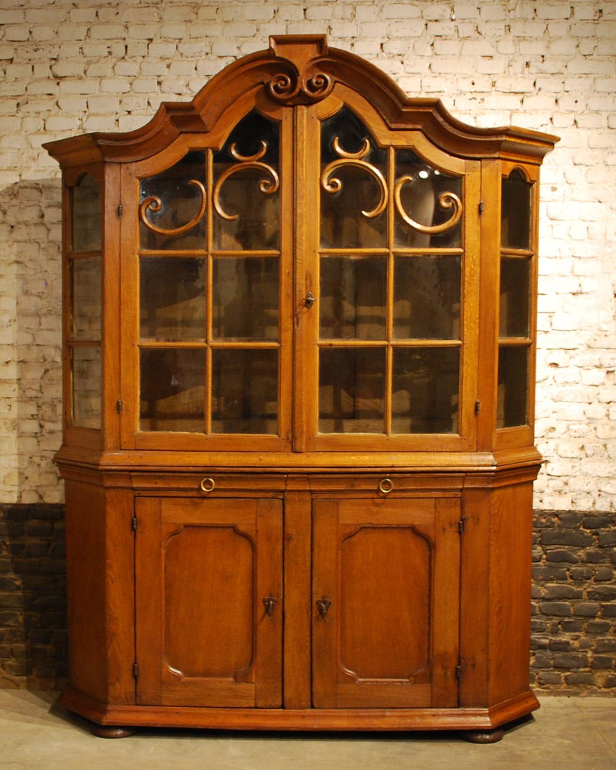 This German Baroque display or kitchen cabinet has a beautiful warm honey color with soft gloss and rich patina.
The cabinet has wide canted corners and a stepped pediment above two glass inset doors in the upper cabinet. Note the small proportion