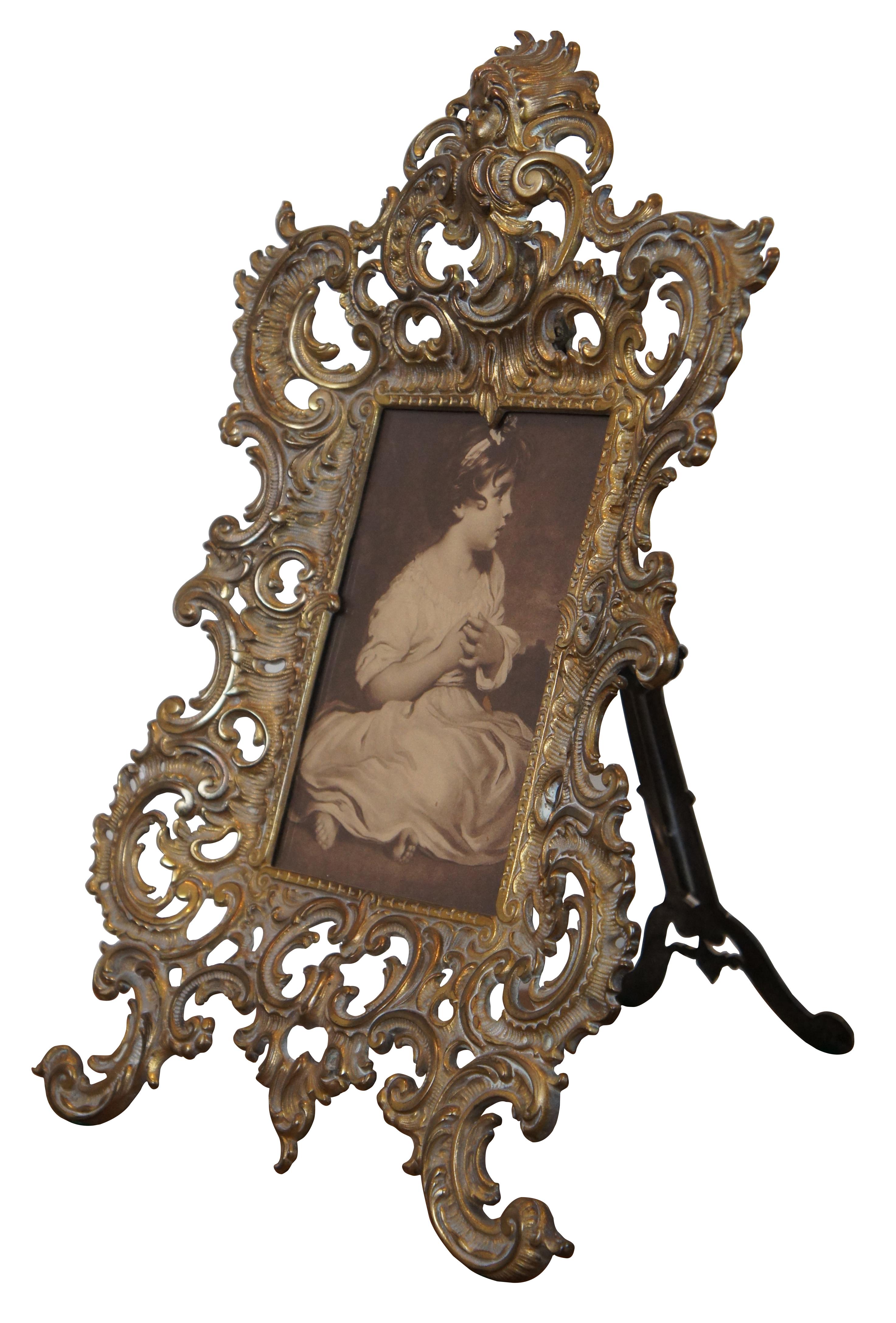 Antique late 19th century reticulated brass easel style picture vanity frame by The National Brass & Iron Works Company (NB & IW) number 2071, featuring a swirling foliate art nouveau design topped with a cherub face. Currently contains a black and