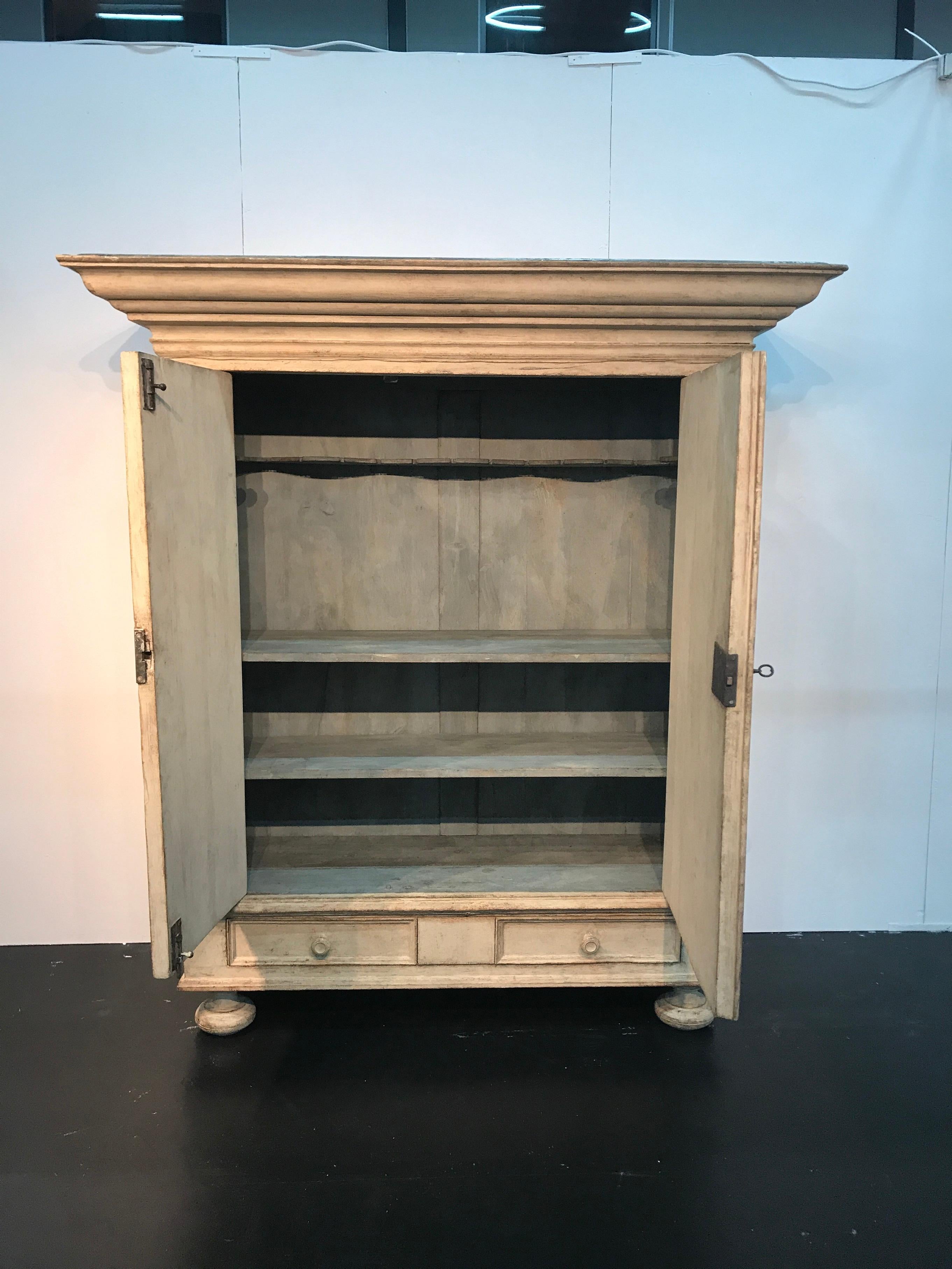 This Baroque armoire features two-doors which open onto shelves and two drawers at the bottom. The exterior is an antique cream color and the interior is grey-blue. It retains the original locks, key, and hardware.