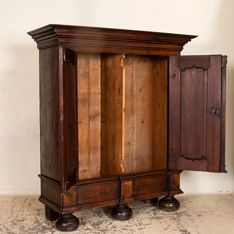 While the large size itself is impressive, it is the heavy Baroque style carving and paneling in the doors and large crown that add to the visual impact of this handsome dark oak armoire. Notice the carved decorative detail above the 3 columns,