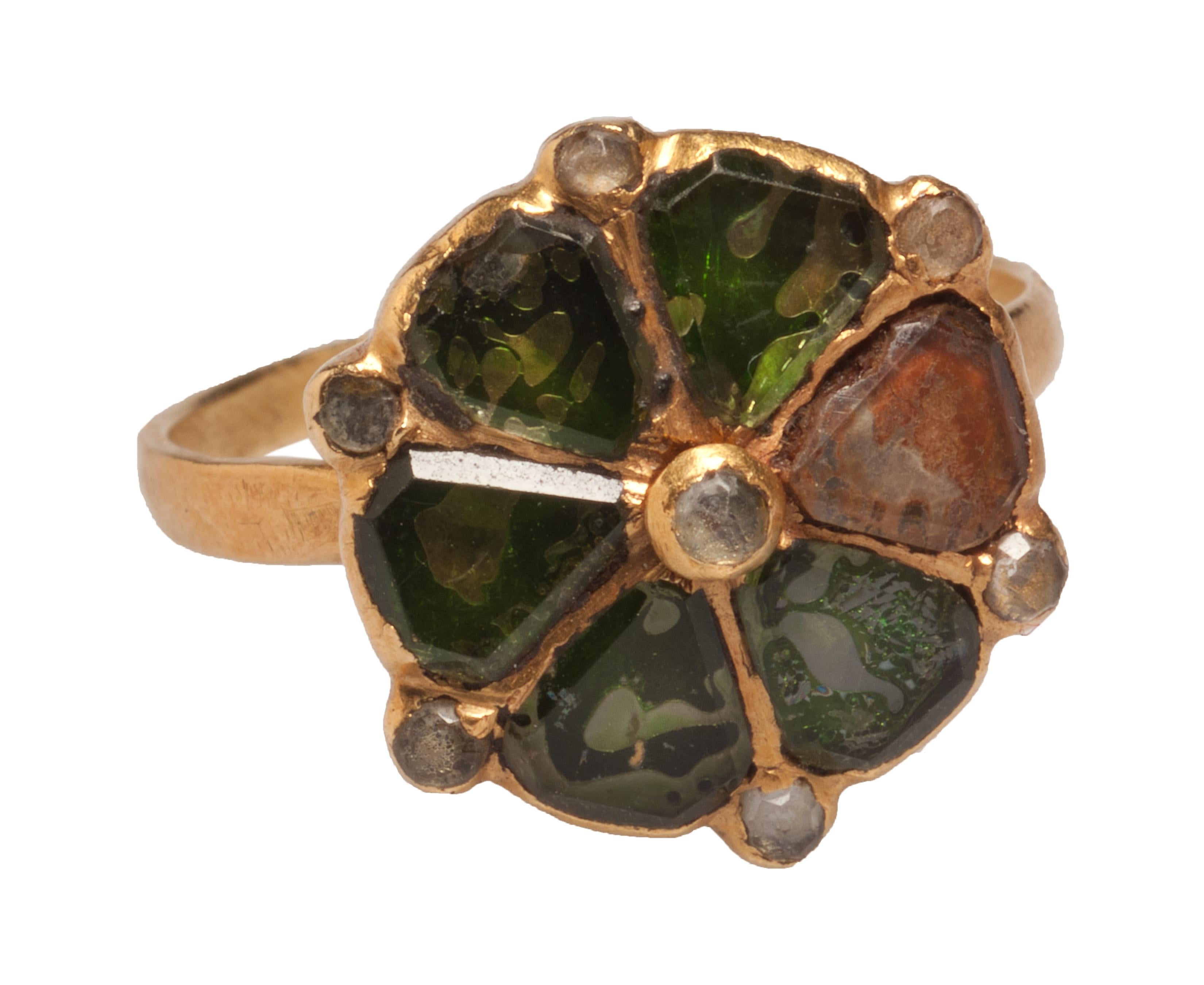 ITALIAN GLASS DECORATIVE RING 
Italy, 17th century  
Gold and foiled glass 
Weight: 4.4 g; circumference 57.6 mm; size: US 8.25, UK Q 

Gold sexfoil bezel set with six diamond-shaped and table cut glass stones over foil. Each petal is interspersed