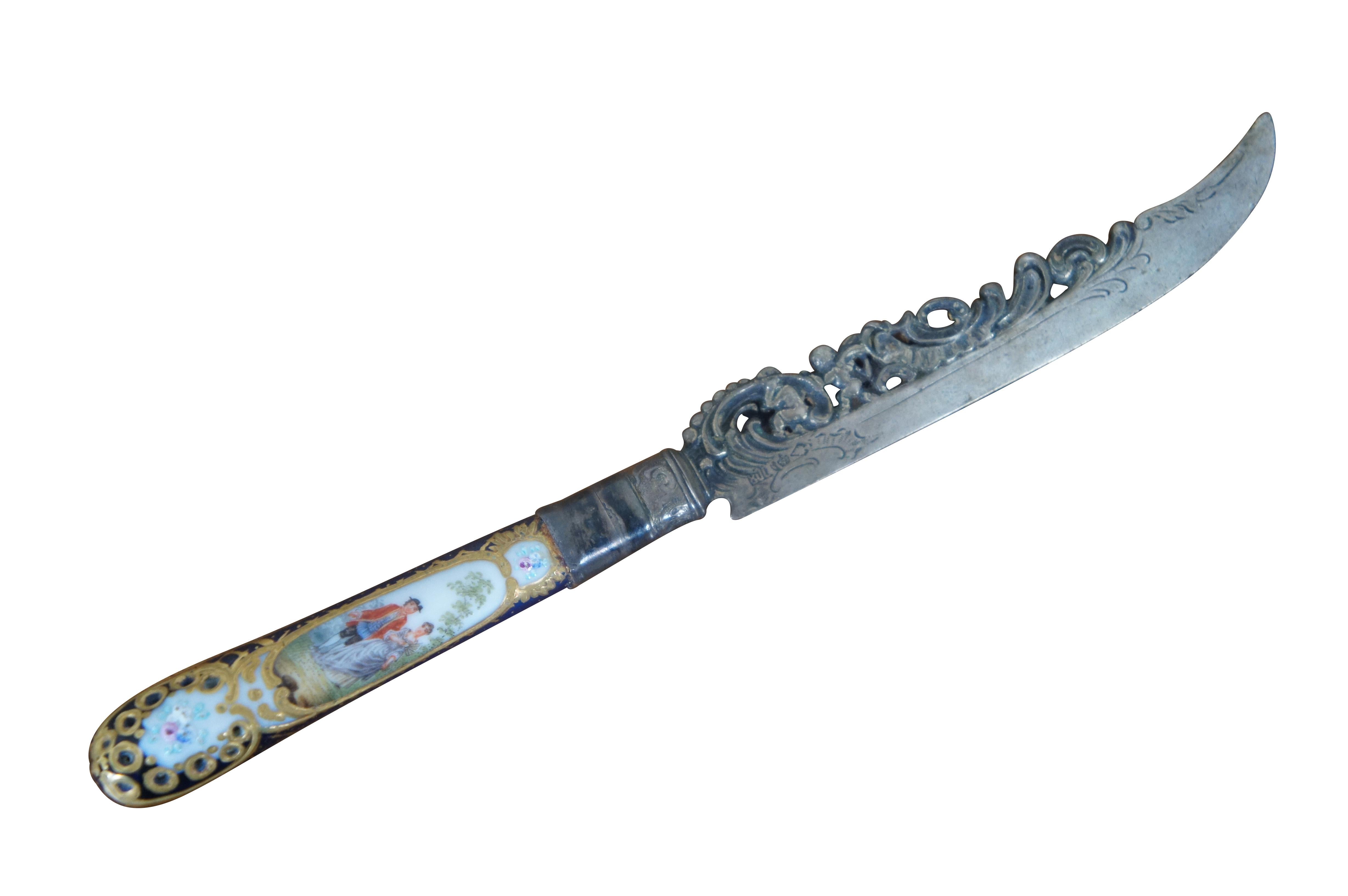 Antique 800 silver porcelain serving knife by Richard Garten, featuring a reticulated baroque blade with figural cherubs and a hand painted cobalt blue and gold accent handle with two colonial couples. 

