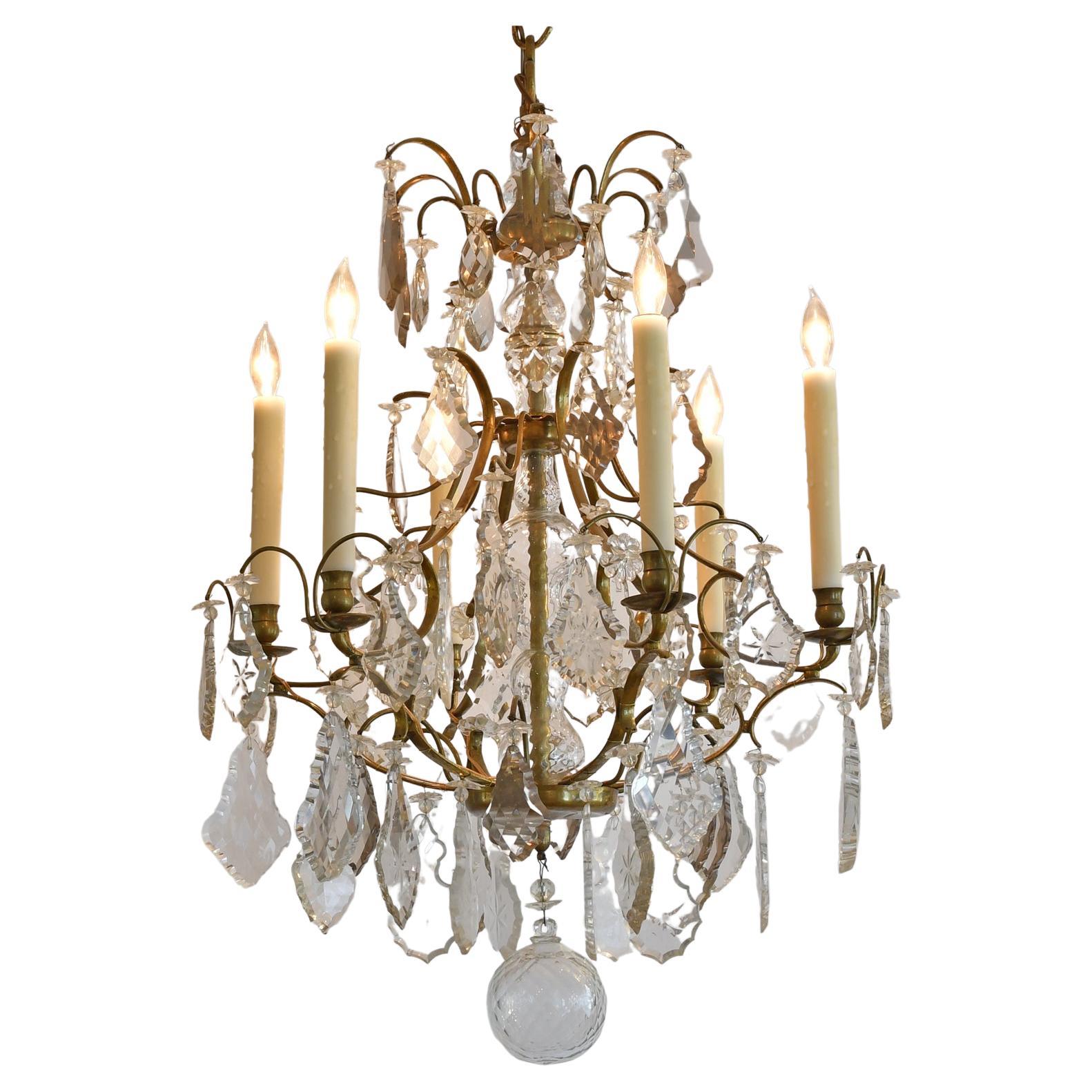 An exquisite mid 19th century baroque-style chandelier with bronze armature offering six (6) lights with finely cut and beveled clear quartz crystal prisms featuring seven different designs, one for each of the tiers, and ranging in shape from leaf,