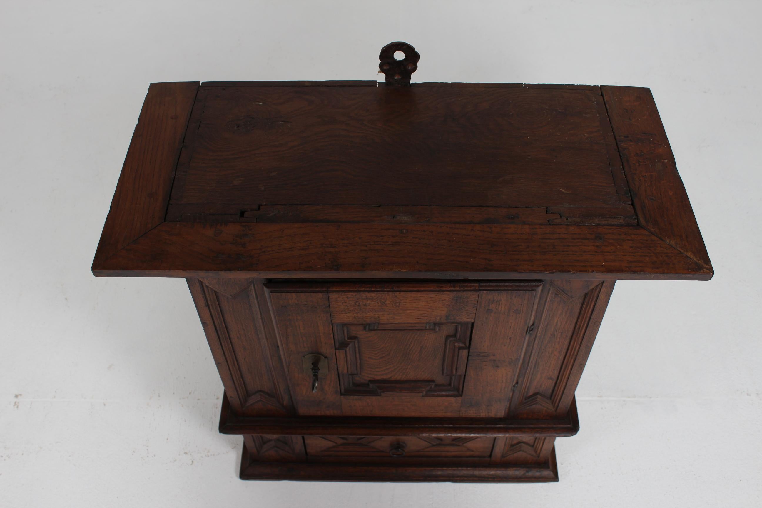 Antique hanging cabinet in baroque style with wood carvings from around 1800.
It is made from solid dark oak and handcrafted by a Danish cabinetmaker at the turn of the 18th century. Behind the door with key are two shelves and underneath a small