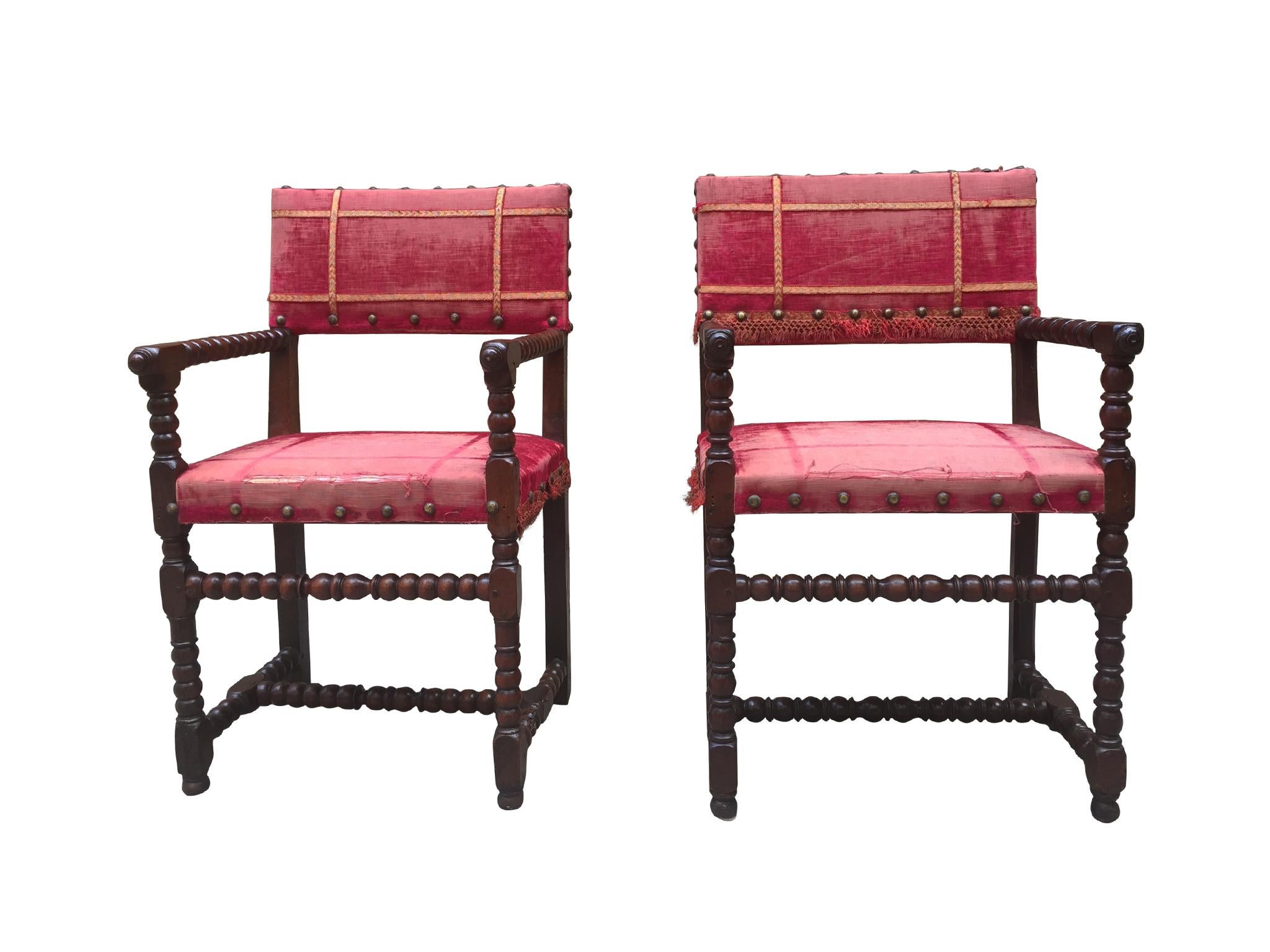 A near-pair set of armchairs in the Baroque-style. 19th century with later additions. The chairs are comprised of walnut wood frame and red velvet upholstery, with yellow grosgrain & studded brass details. The construction of the chairs is a Classic