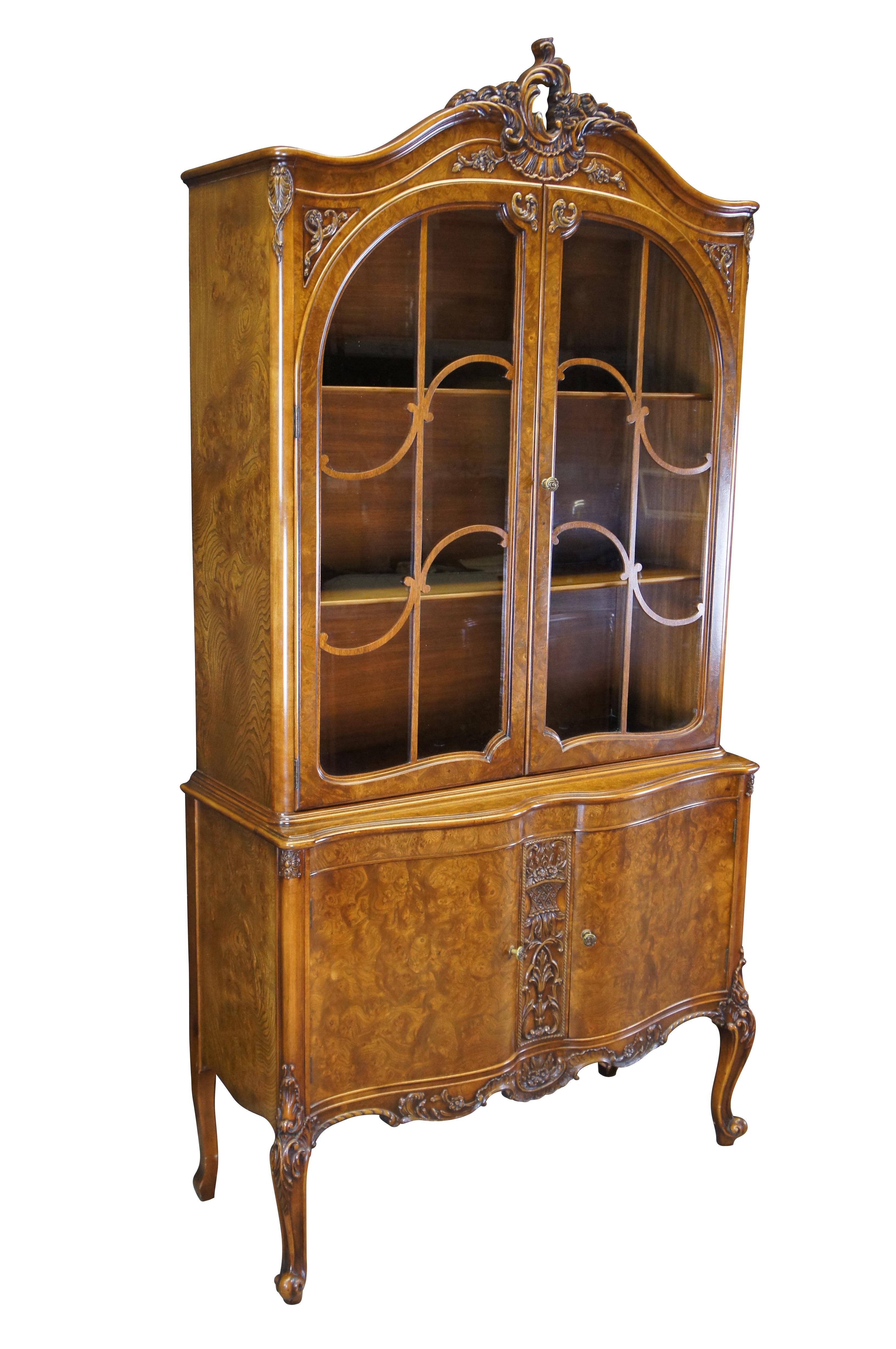 Antique Batesville Cabinet Co French Provincial Louis XV china curio cabinet / cupboard.  Made of Carpathian cluster elm burl featuring upper cabinet with serpentine floral cartouch crown and fretwork doors over lower cabinet with carved acanthus