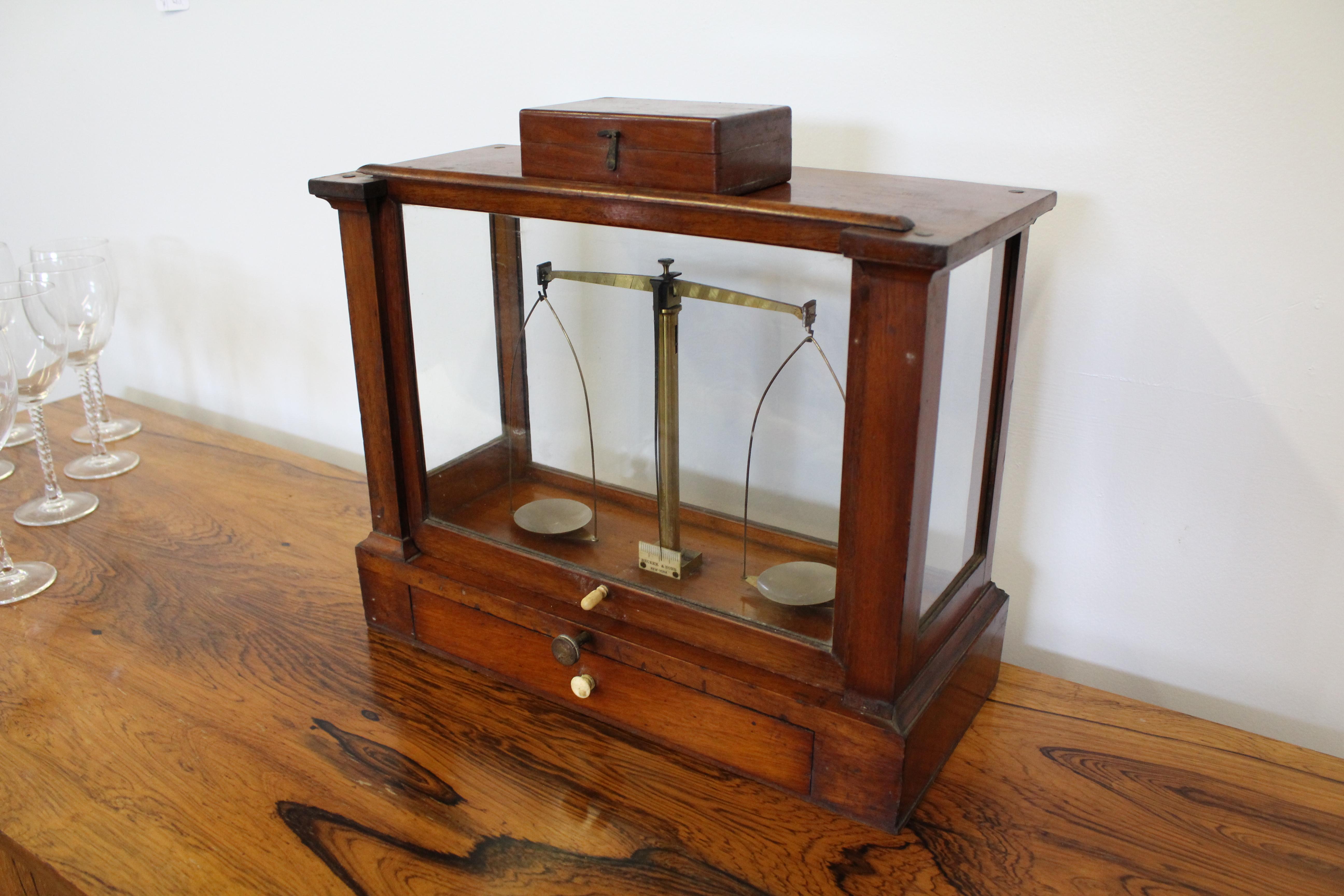Offered is a rare, antique apothecary scale made by Becker & Sons of New York, circa 1903. The scale is housed inside a glass case with a mahogany frame and pull out drawer. There is a glass unit with sliding window on front side as well as the back