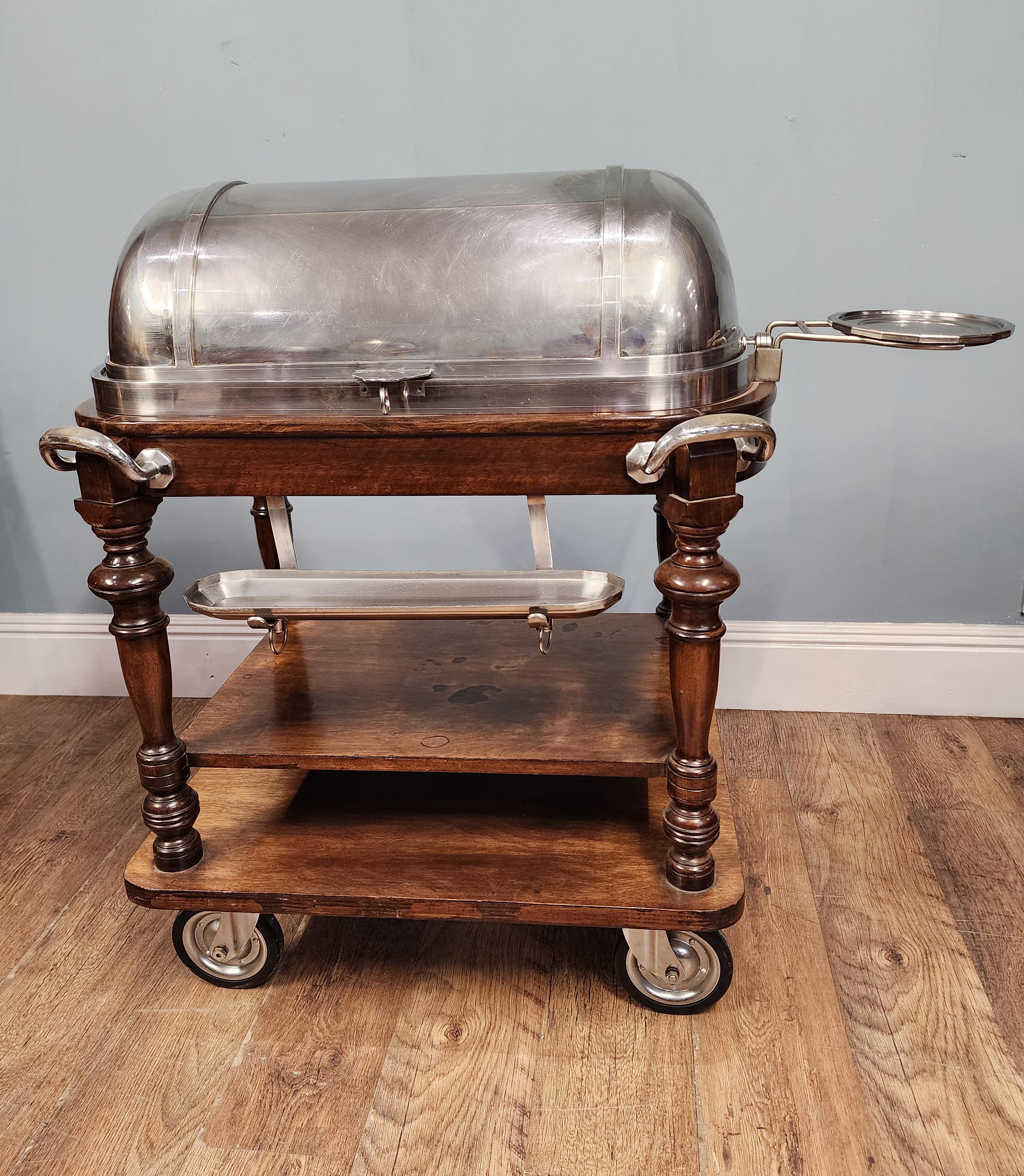 Magnífico carro de servicio antiguo equipado con un gran plato hondo / chafing dish plateado abovedado, ideal para carveries, ambientes de hospitalidad o exhibición teatral en comedores
Se desplaza fácilmente sobre ruedas y tiene una placa lateral