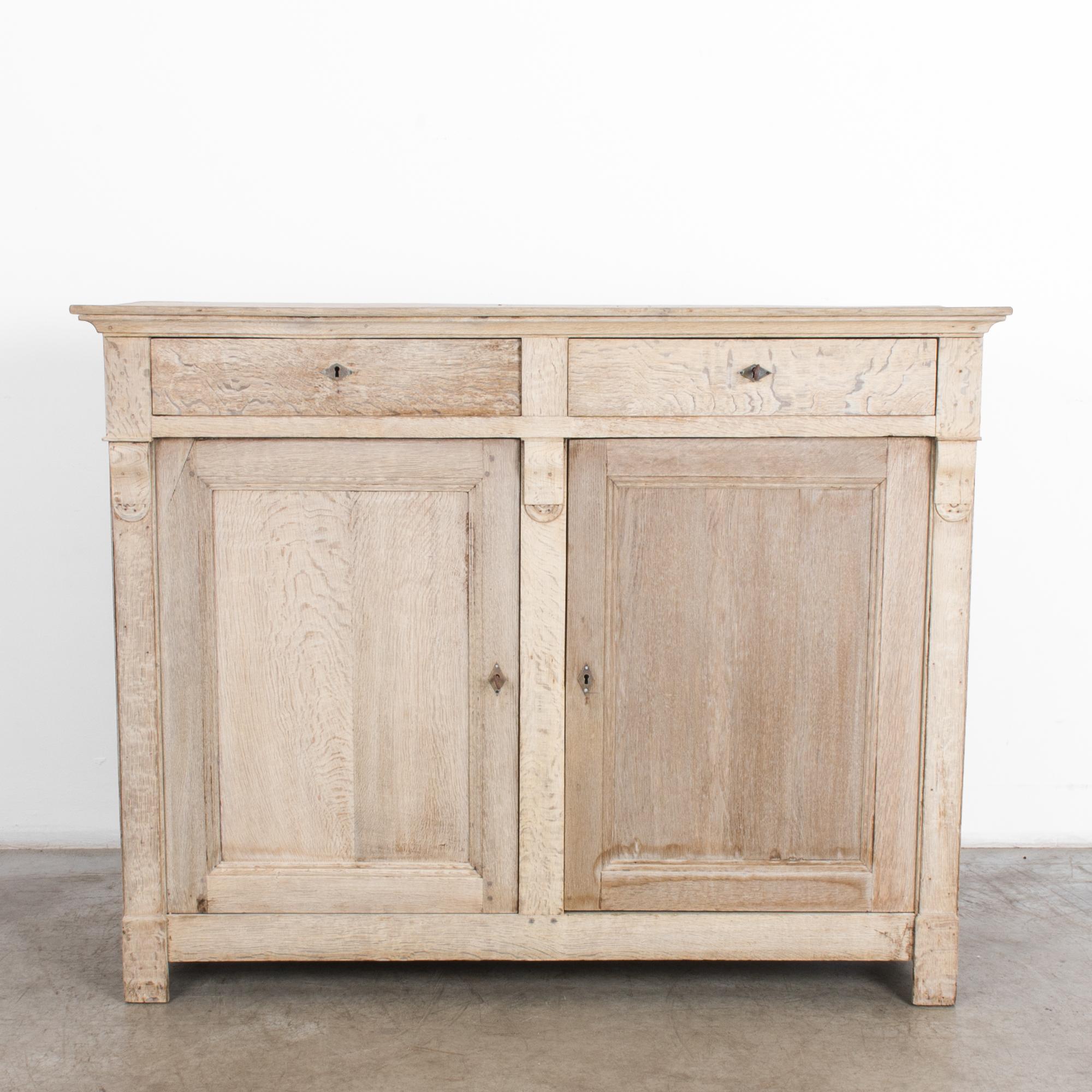 Made in Belgium in the 1880s, this oak buffet features two doors and two drawers. A simple shape and natural finish recall the spartan interior of the country home, with a subtle elegance. The Charles X silhouette nods to formal fashion. Restored in