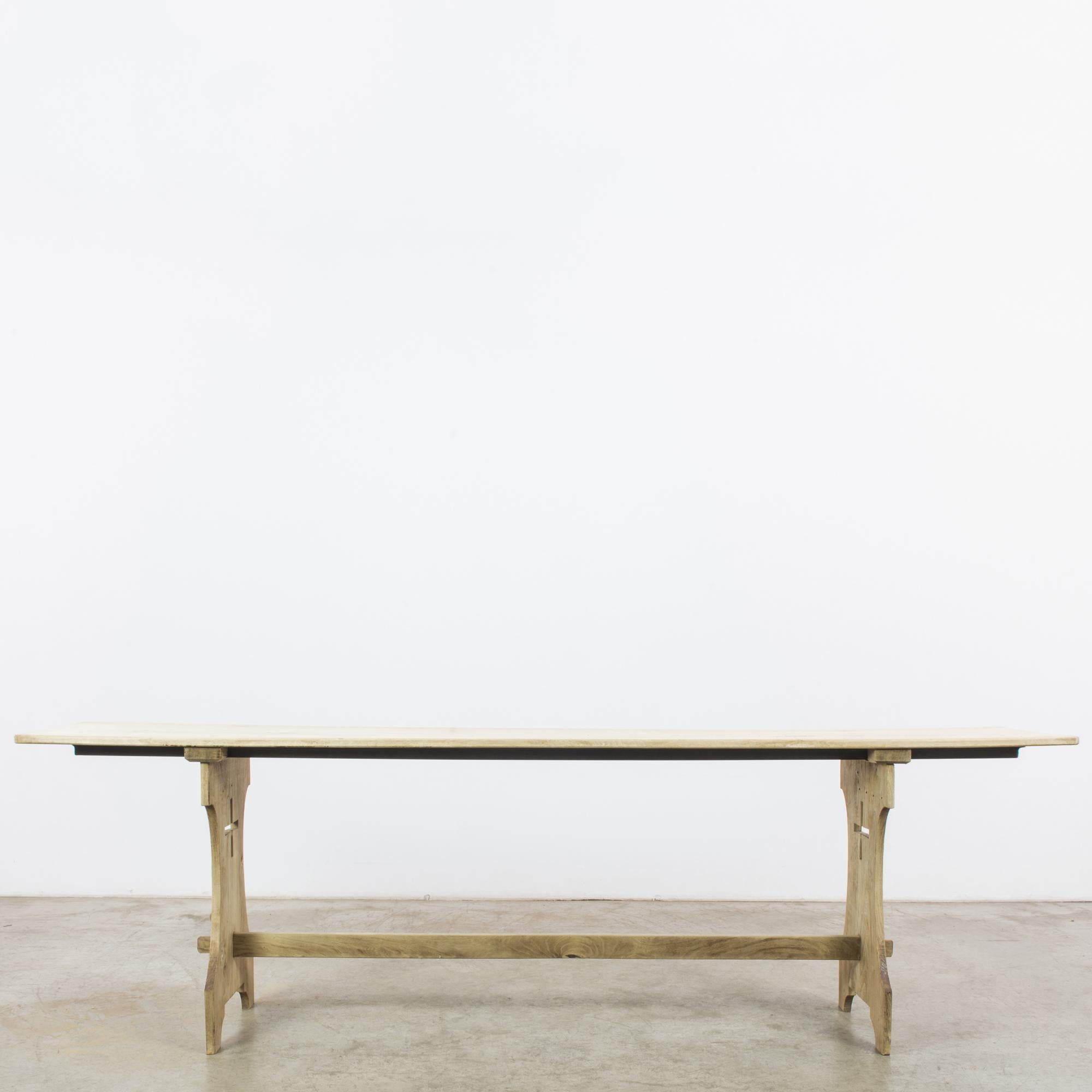 This antique wooden table was made in Belgium. A simple and functional trestle table, it features an elongated tabletop and slim panels. The cross cutout of the posts offers a contrast with the contoured sides, while the traditional joinery
