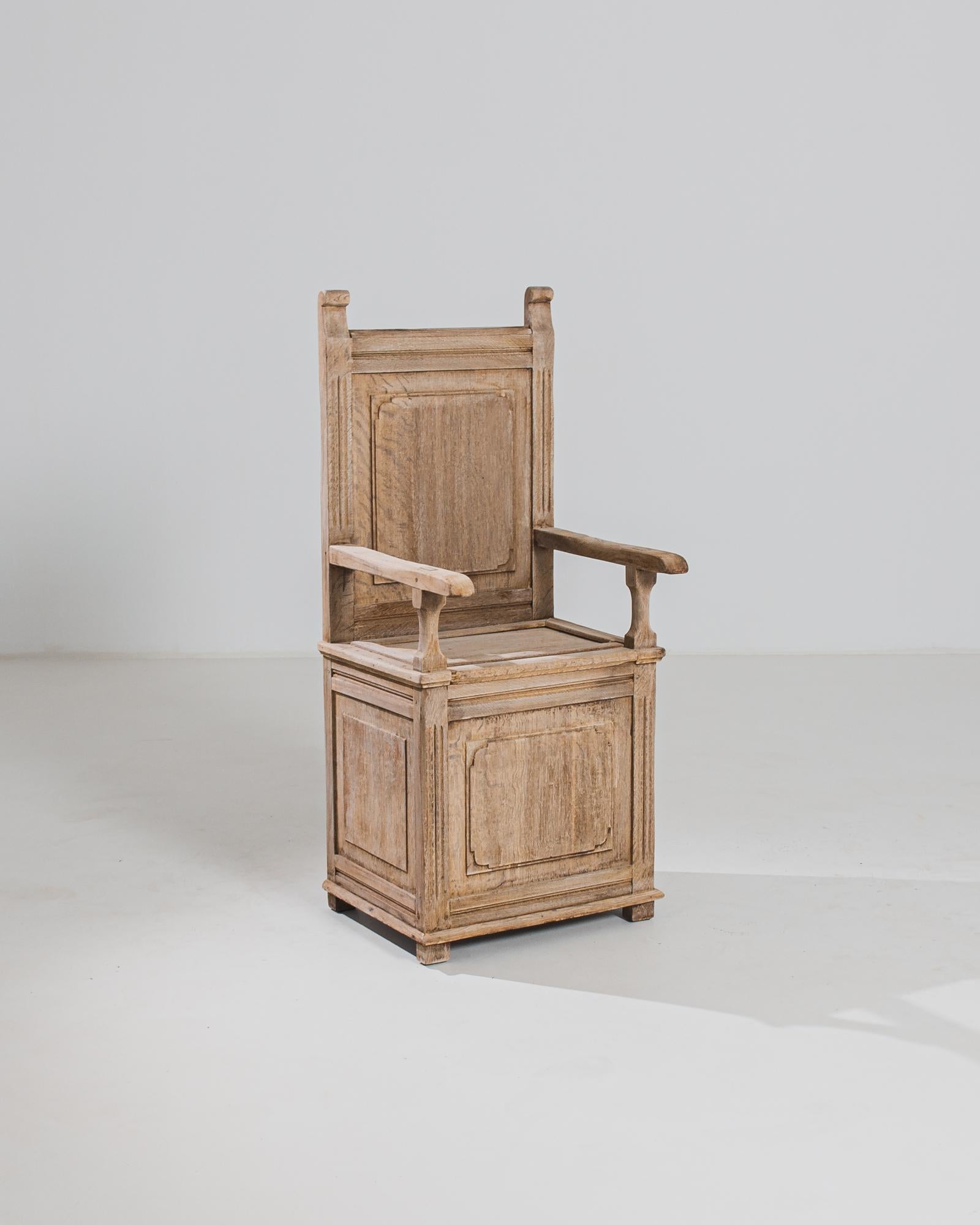 Made in Belgium, this antique bleached oak armchair offers a stately and dignified presence with its box seat, upright back, and horizontal armrests. Alongside its rustic tone, the subtle curves on the stiles and molding soften its rectilinear