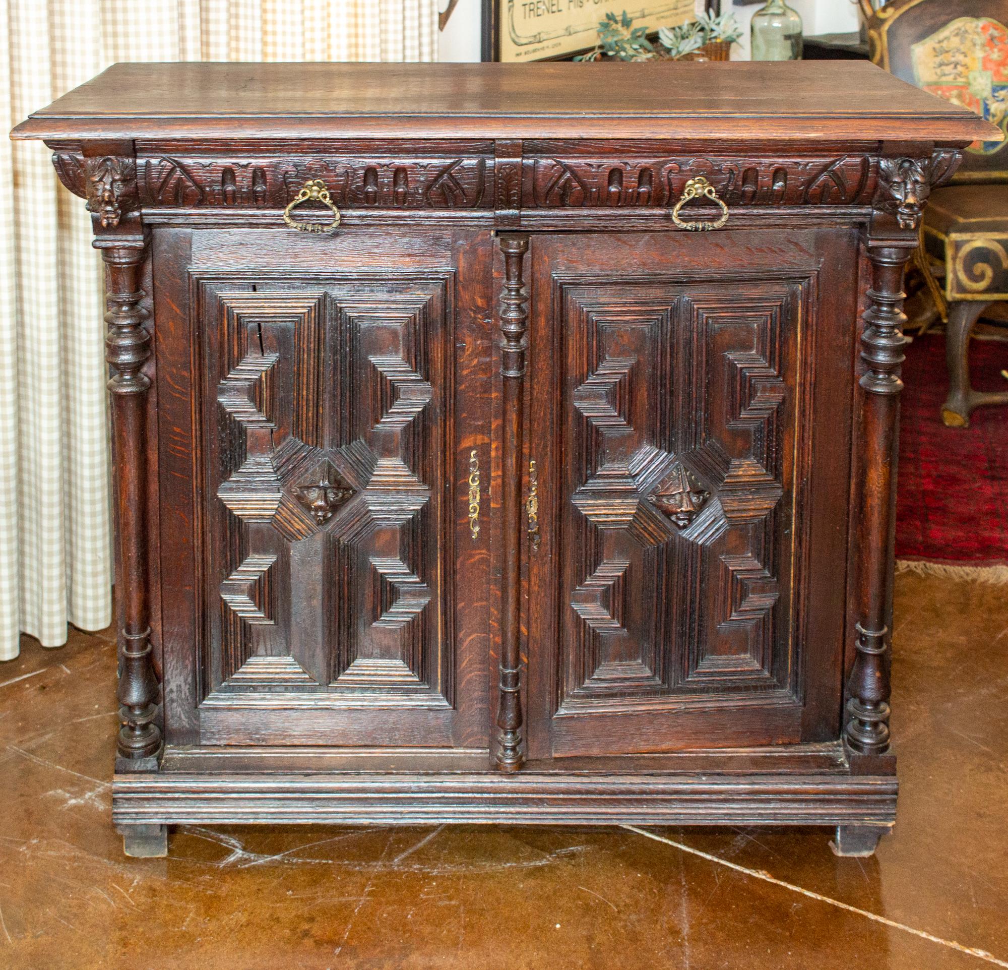 This antique Belgian buffet features ornate geometric carvings and a beautiful, rich, patinated wood finish. The doors have head-shaped 