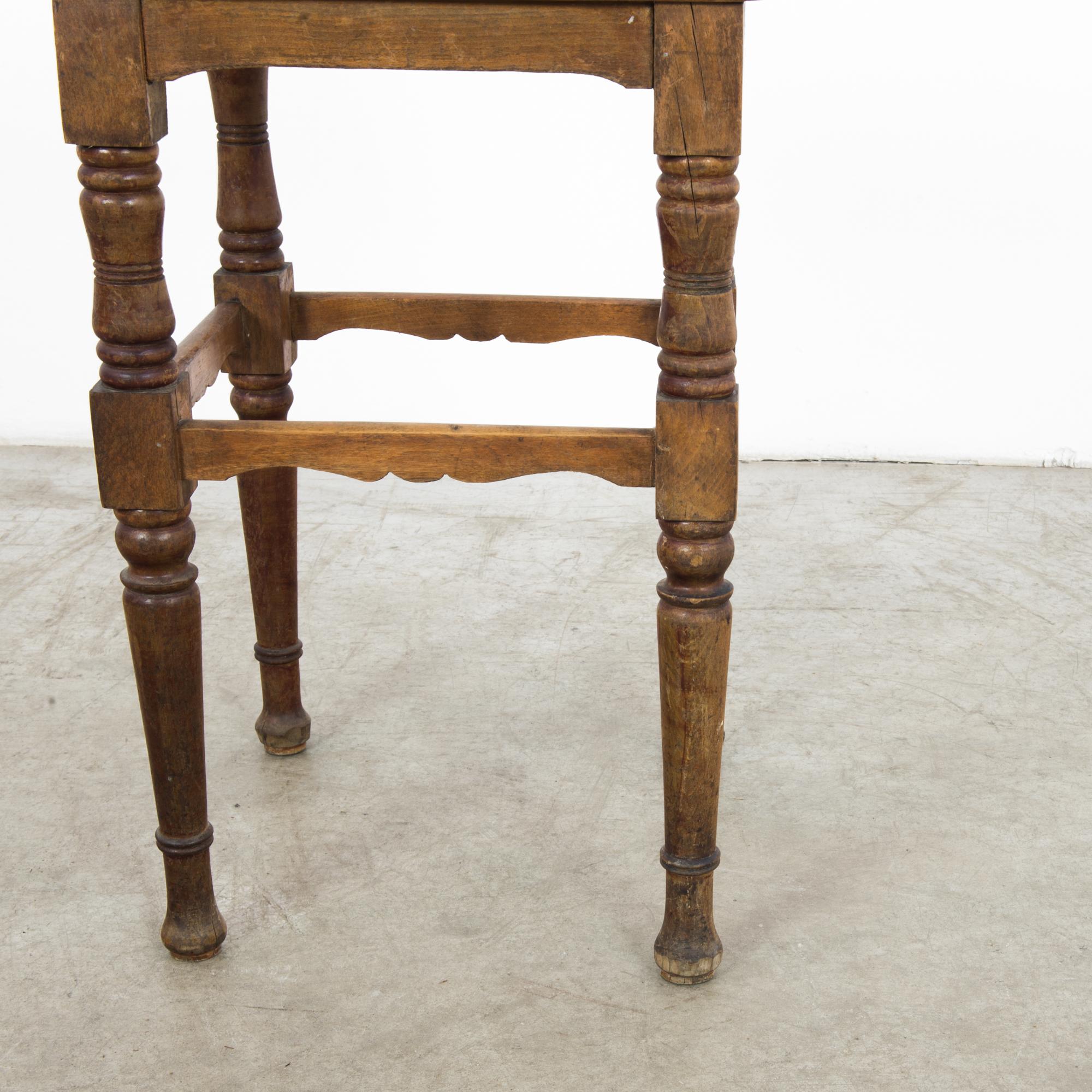 This wooden stool was made in Belgium and features a slightly tilted square seat with a cane center. It is supported on four turned legs with scalloped stretchers. With its warm tone and timeworn patina, the stool will impart a rustic, farmhouse