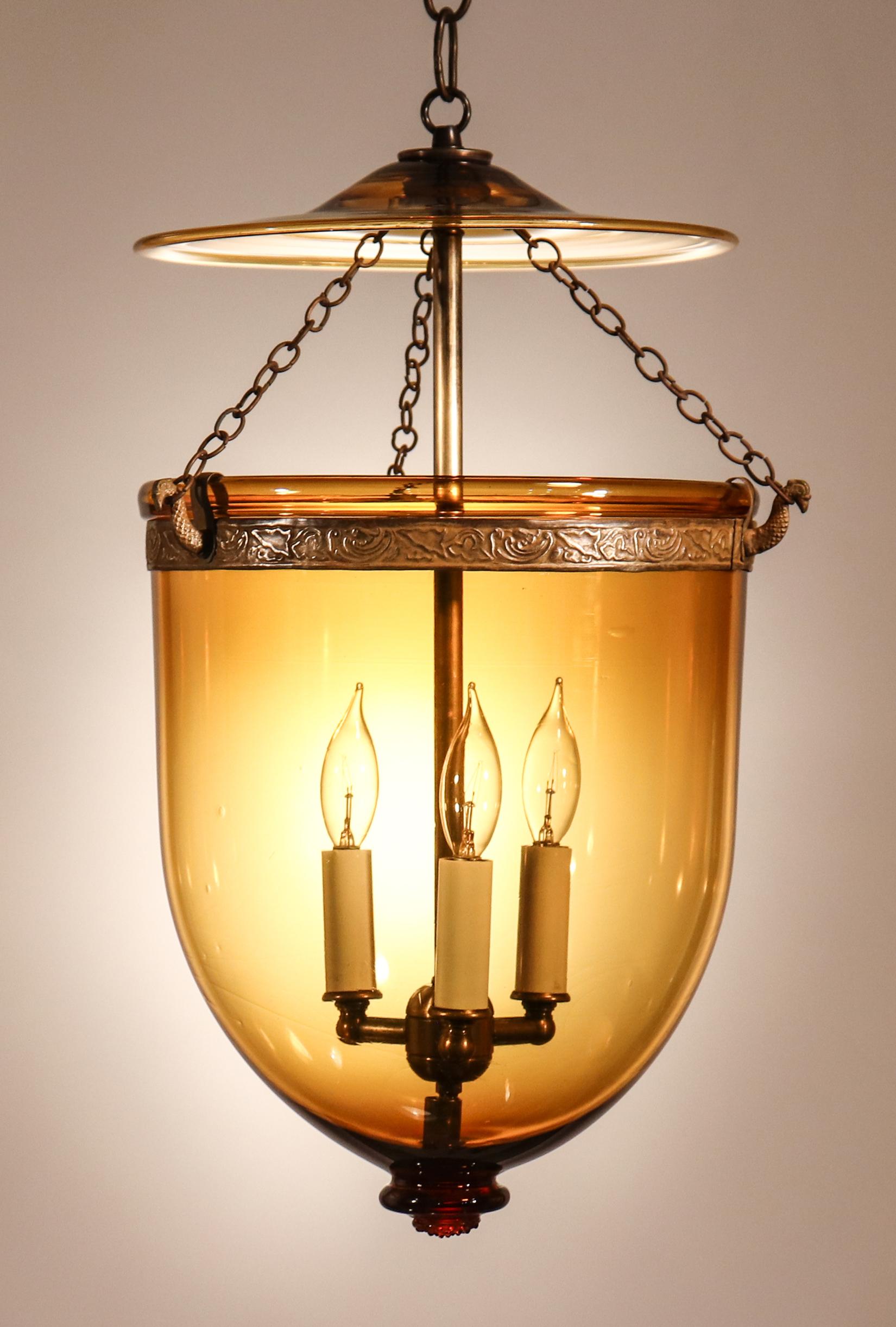 A rich amber-colored bell jar lantern with its original smoke bell and a decorated brass band with embossed vine design. The quality of this circa 1880 lantern is excellent, with desirable air bubbles and swirls in the hand blown glass. The pendant