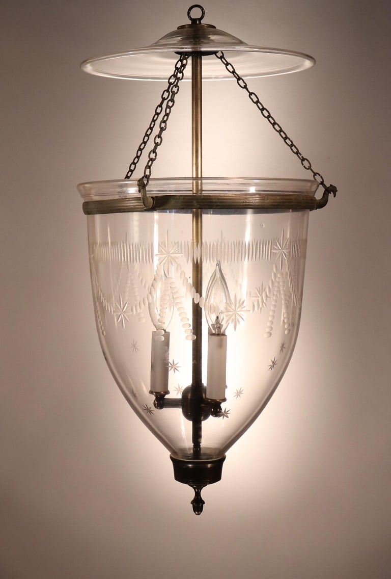 An antique English bell jar lantern featuring outstanding quality hand blown glass and an etched Federal-style design, circa 1860. This classic pendant features its original smoke bell and rolled brass band. The brass finial/candleholder base was
