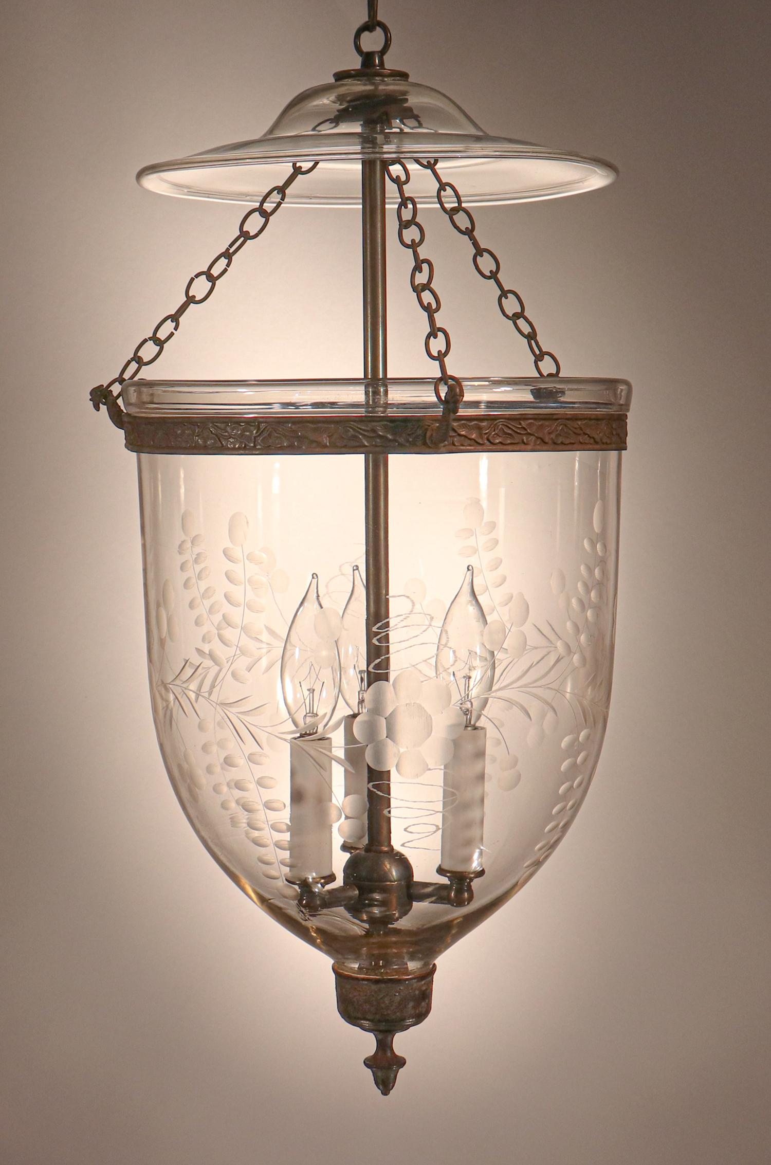 An outstanding antique English bell jar lantern with a finely etched floral motif. This circa 1850 lantern features very good quality hand blown glass replete with desirable swirling, as well as an original embossed brass band and chains. The
