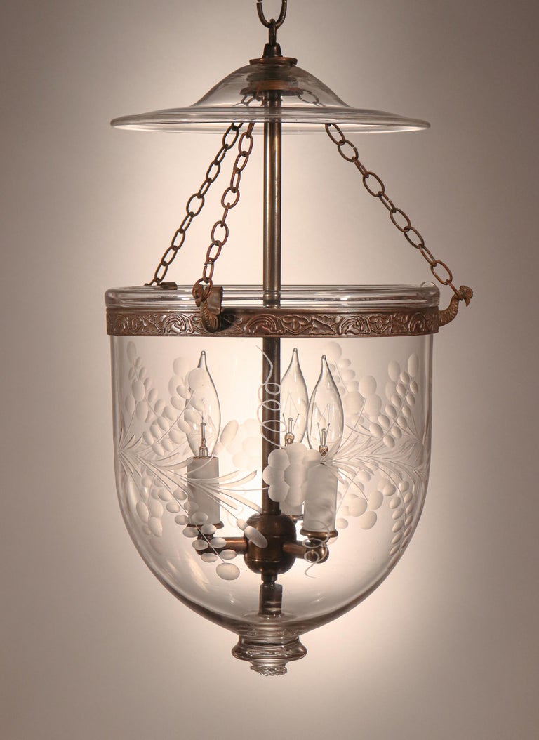 A lovely antique English hand blown glass bell jar lantern with an etched floral motif, circa 1880. The lantern has an attractive full form for its relatively diminutive size. It features its original glass smoke bell/lid. The embossed brass band,