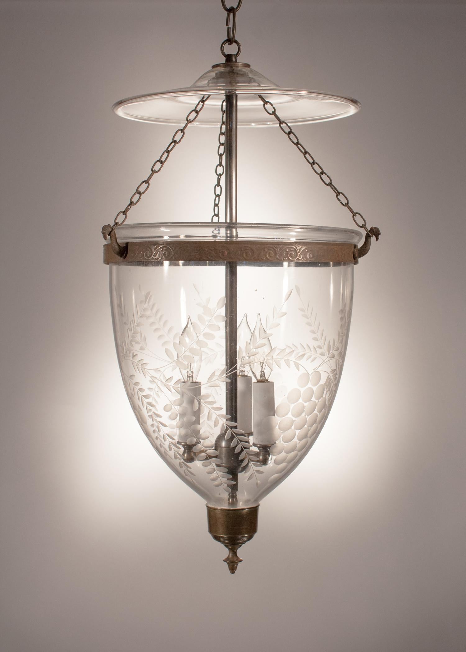An antique English hand blown glass bell jar lantern with lovely form and a complementary etched grape motif. This circa 1870 bell jar pendant has its original glass smoke bell/lid and brass finial. The embossed brass band and chains have been