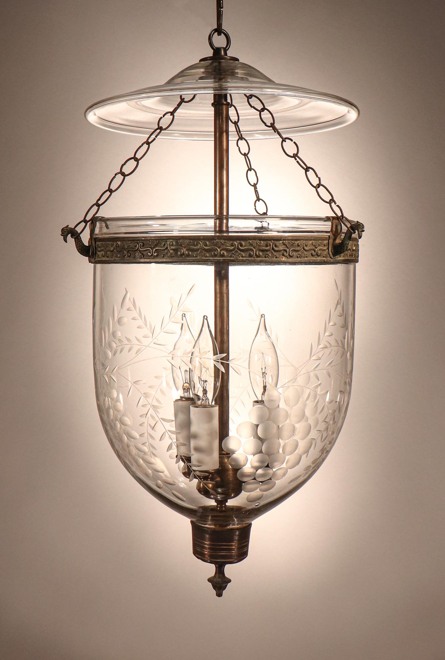 A lovely hand blown glass bell jar lantern from England with an etched grape motif. This circa 1870 lantern features its original embossed brass band, strands of chain, and smoke bell/lid. The pendant's brass finial, which originally held a candle,