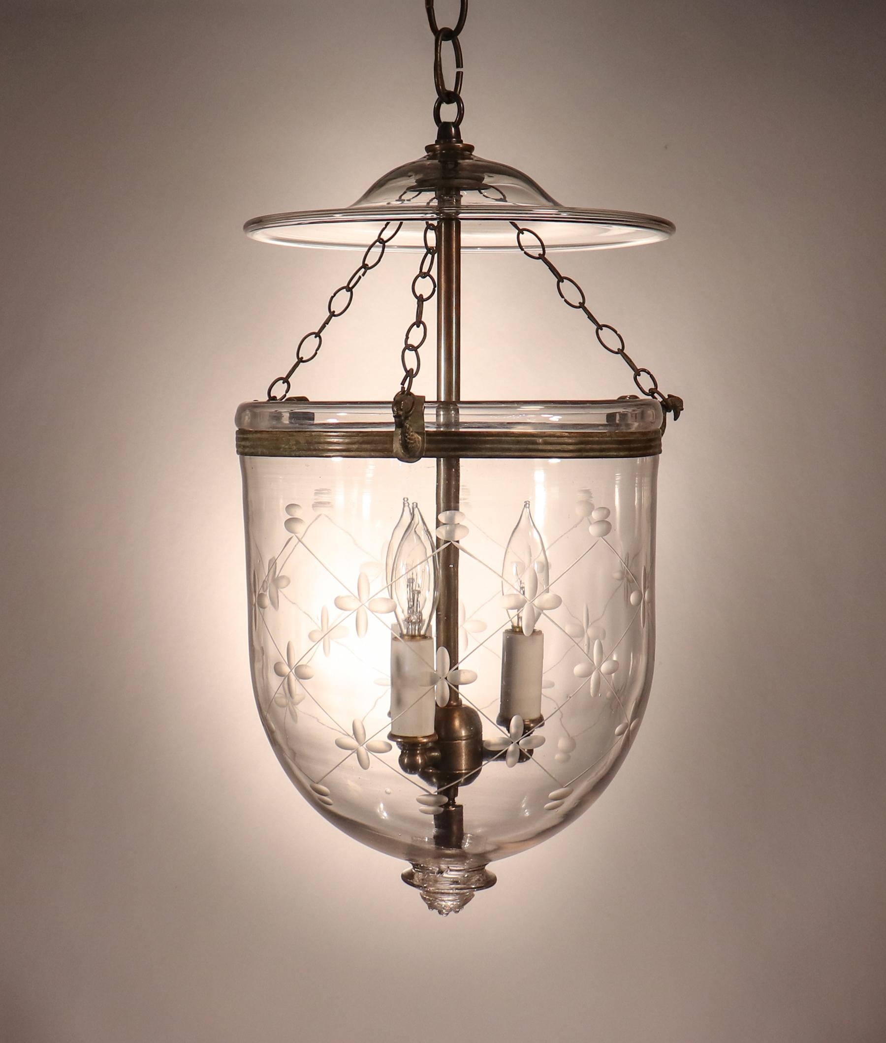 A charming English bell jar lantern, circa 1870, with its original rolled brass band and chains. The quality of the lantern's handblown glass is excellent, with tiny, desirable air bubbles and an attractive glass pontil. The pendant's etched trellis