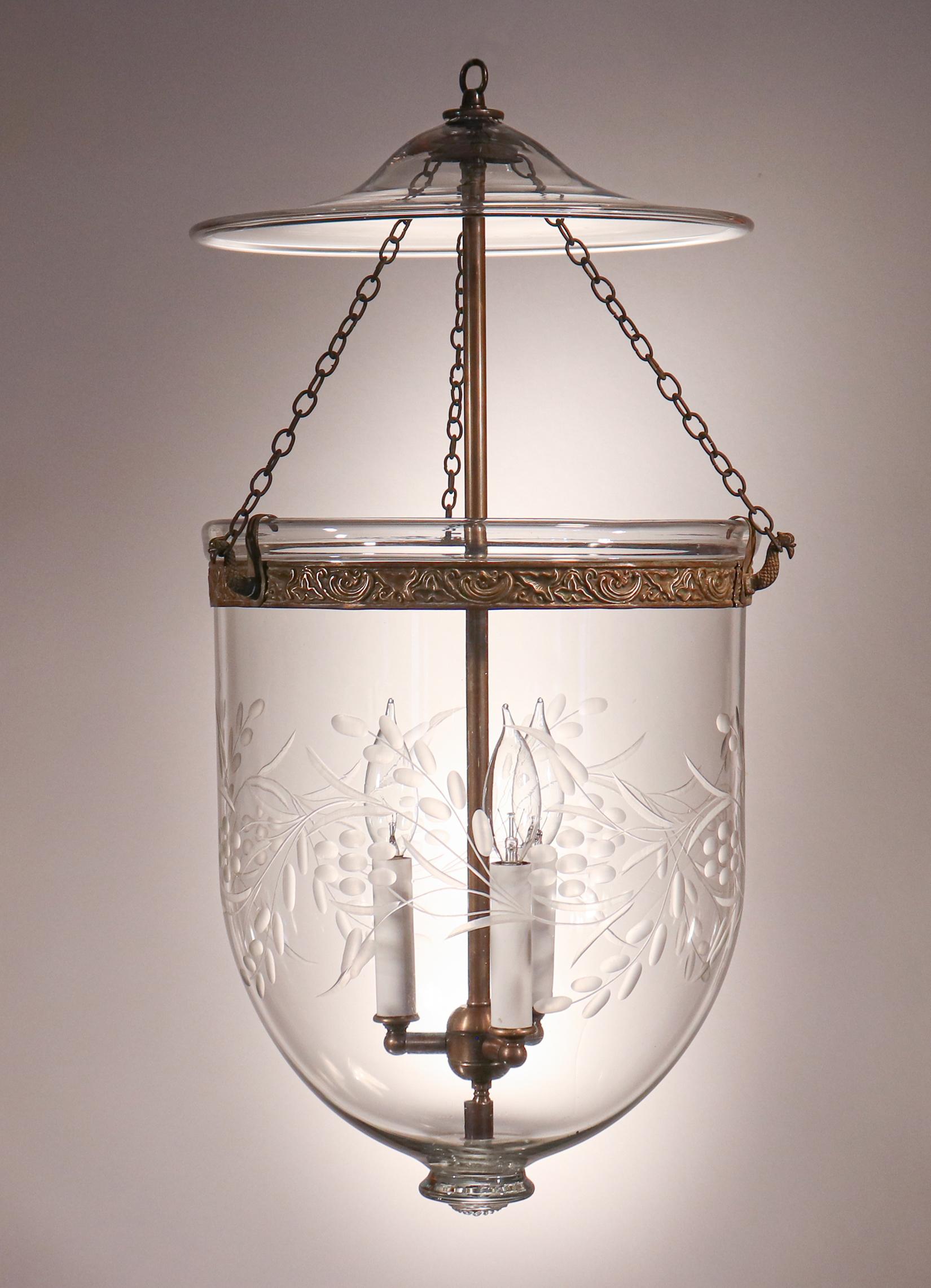 Antique bell jar lanterns of this quality and size are difficult to find. This especially lovely hand blown glass English pendant features a finely etched vine and berry motif and an original brass band with embossed floral design. The lantern has