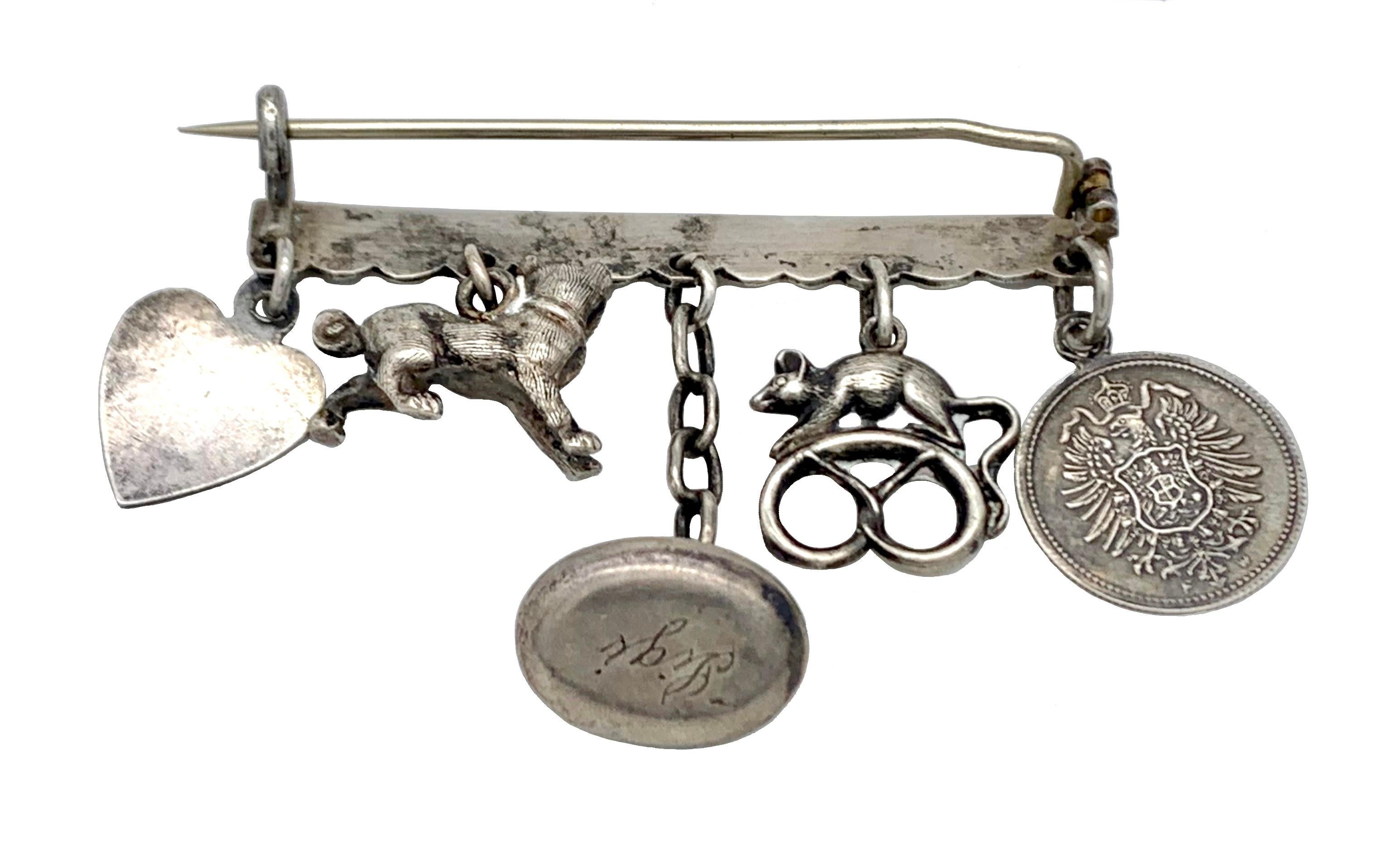 This charming silver brooch features a collection of articulated charms : a medal with Marie inscribed, a Mouse sitting on a pretzel, a bed pan with the name ski inscribed, a cat and a heart with the inscription' Behüt dich Gott' (may god protect