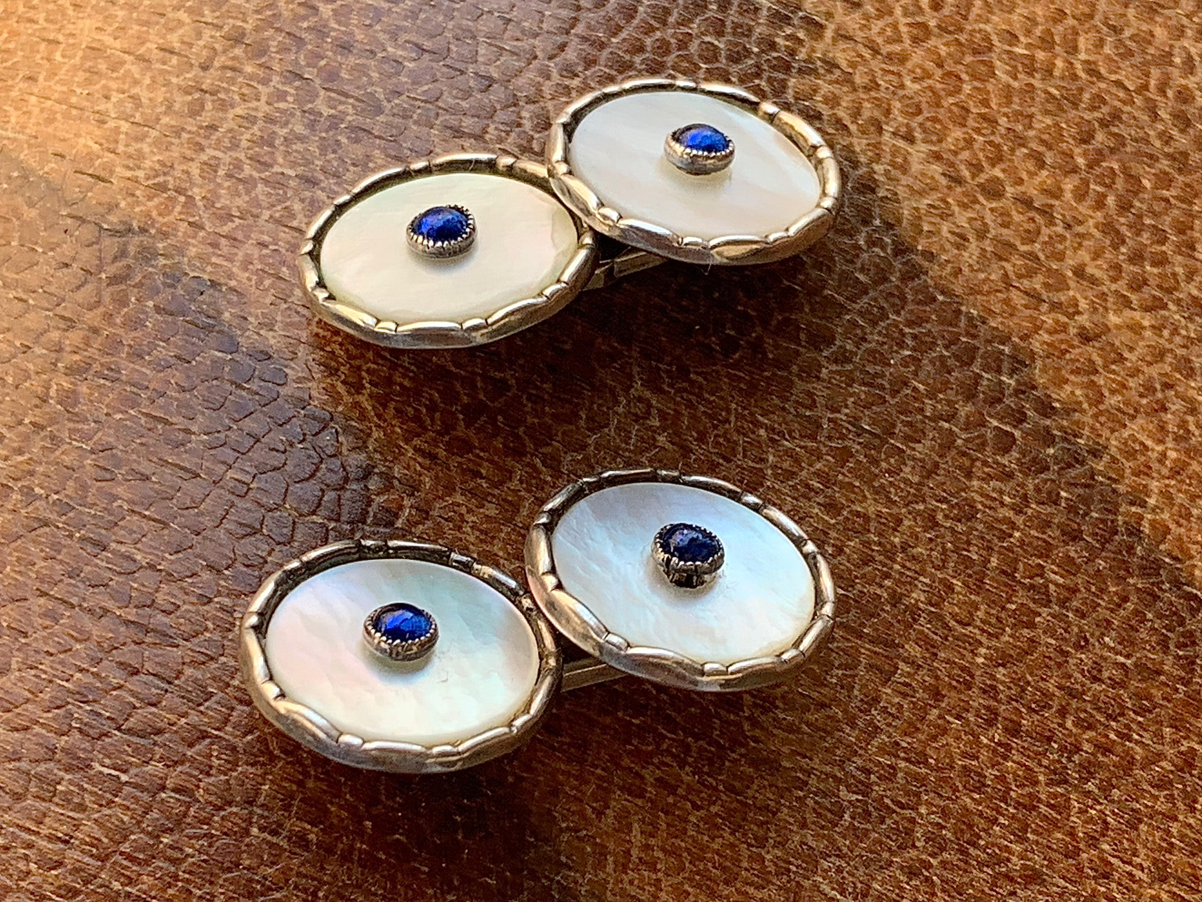Questi gemelli della Belle Époque sono stati creati all'inizio del 1910ca.  I dischi rotondi di madreperla sono incastonati in montature ornamentali d'argento. Al centro di ogni disco c'è un cabochon di pasta blu. Due dei cabochon presentano piccole
