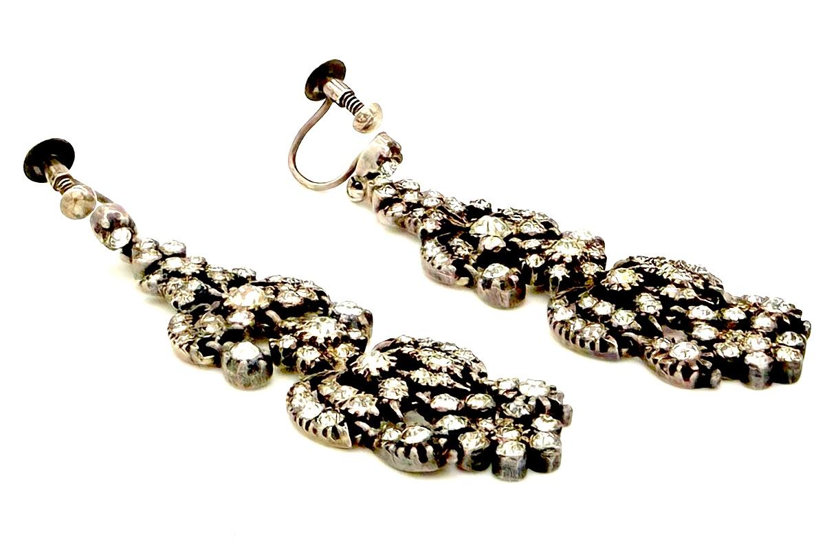 This stiking pair of chandelier dangle earrings was created between 1910 and 1920 in the 18th century revival taste. The earrings are  made out of silver and set with paste. They are in fine original condition including the screw fittings screw