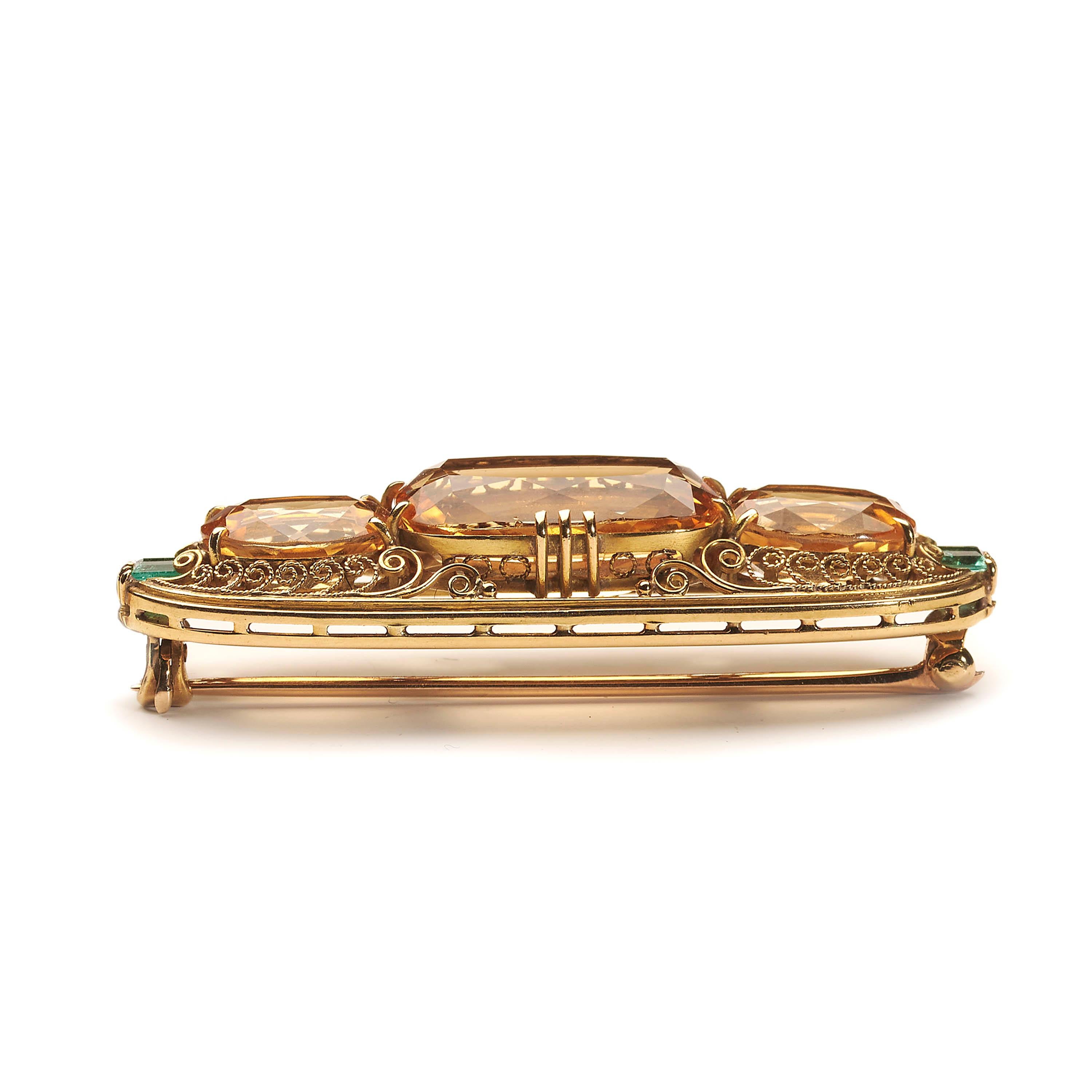 An antique, Belle Époque style, Tiffany & Co. imperial topaz and emerald brooch, set with a trio of faceted, cushion-cut and faceted, oval-cut imperial topaz, with an estimated total weight of approximately 26.5 carats, accented by a step cut