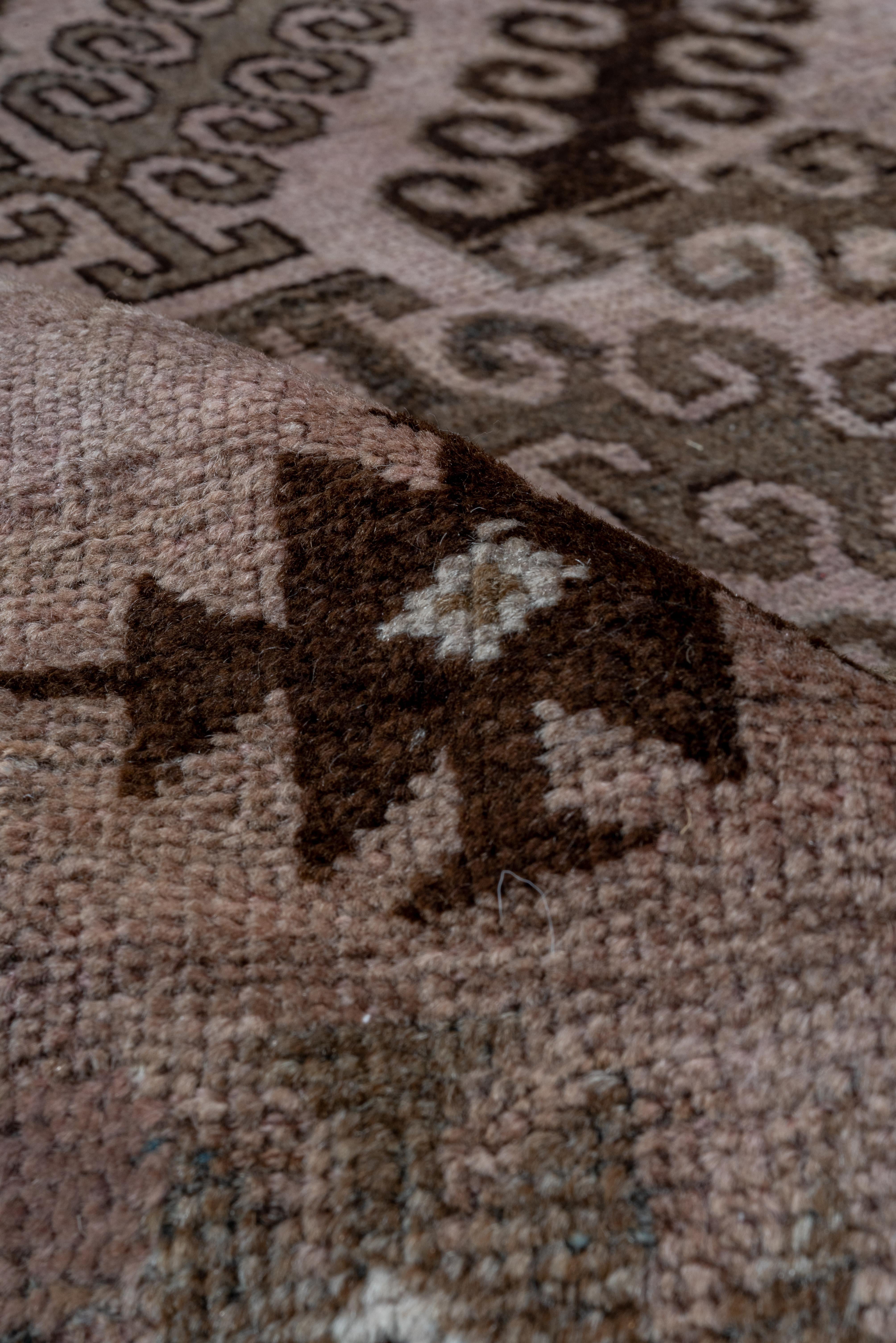Ce tapis antique Belouch présente un remarquable treillis central de médaillons de diamants imbriqués en noyer foncé, encadré par de multiples bandes de garde remplies de fins motifs tribaux. Le fond rosé adoucit la géométrie audacieuse, conférant à