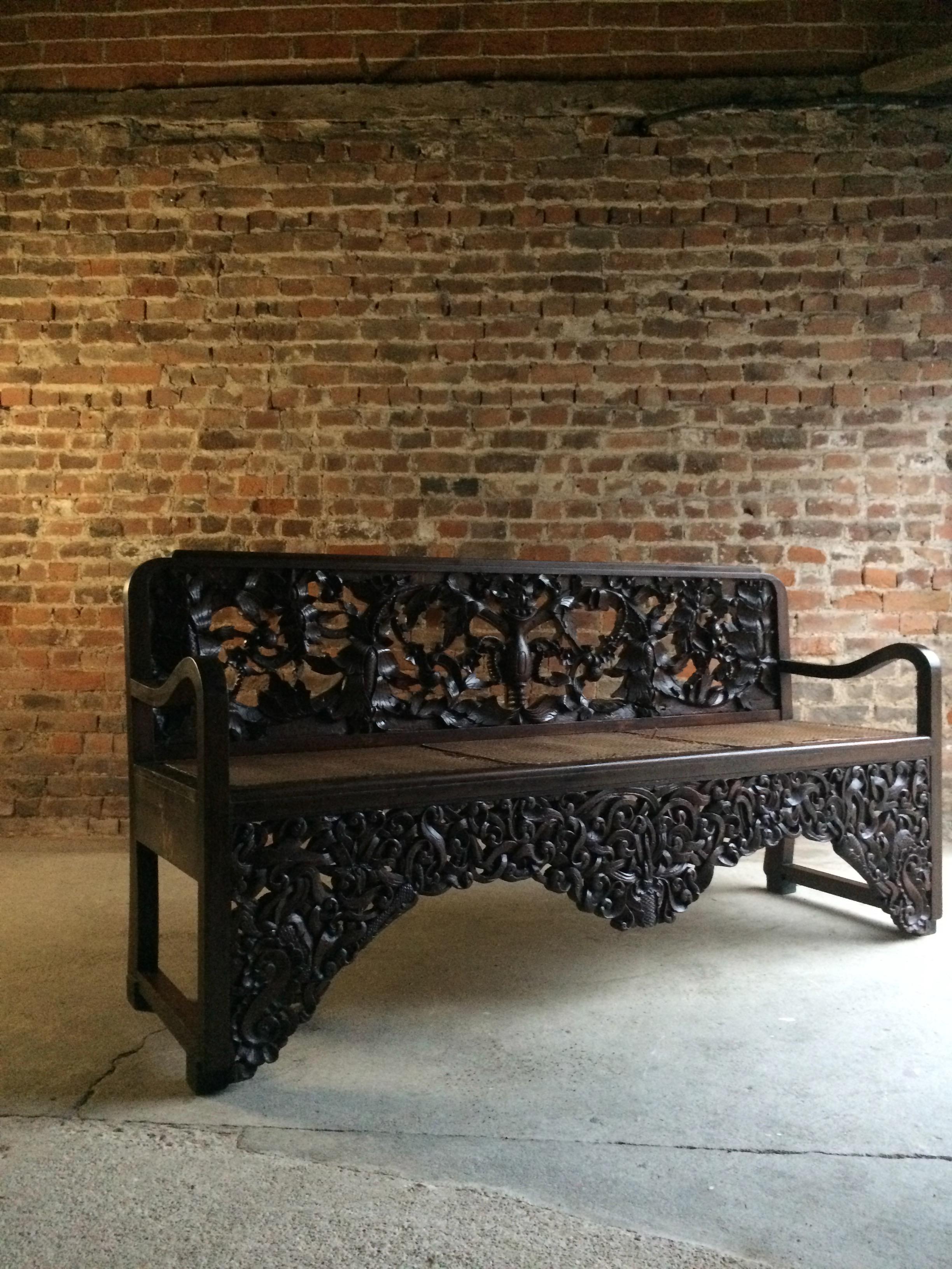 A magnificent early 20th century oriental hardwood cane seated hall bench circa 1900, the back and apron profusely carved with entwined scrolling lotus, raised on heavily carved legs.

Condition report: The bench is offered in good antique