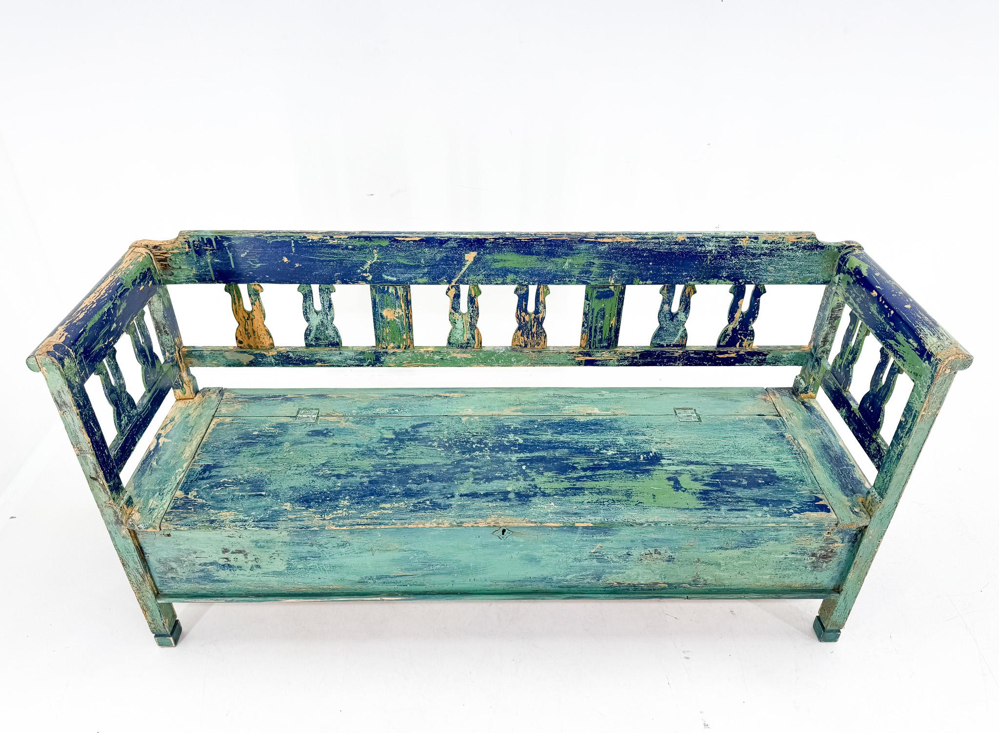An antique bench that has undergone several coats of paint in the past after the partial removal of which has resulted in this beautiful patina. The bench has newer hinges.