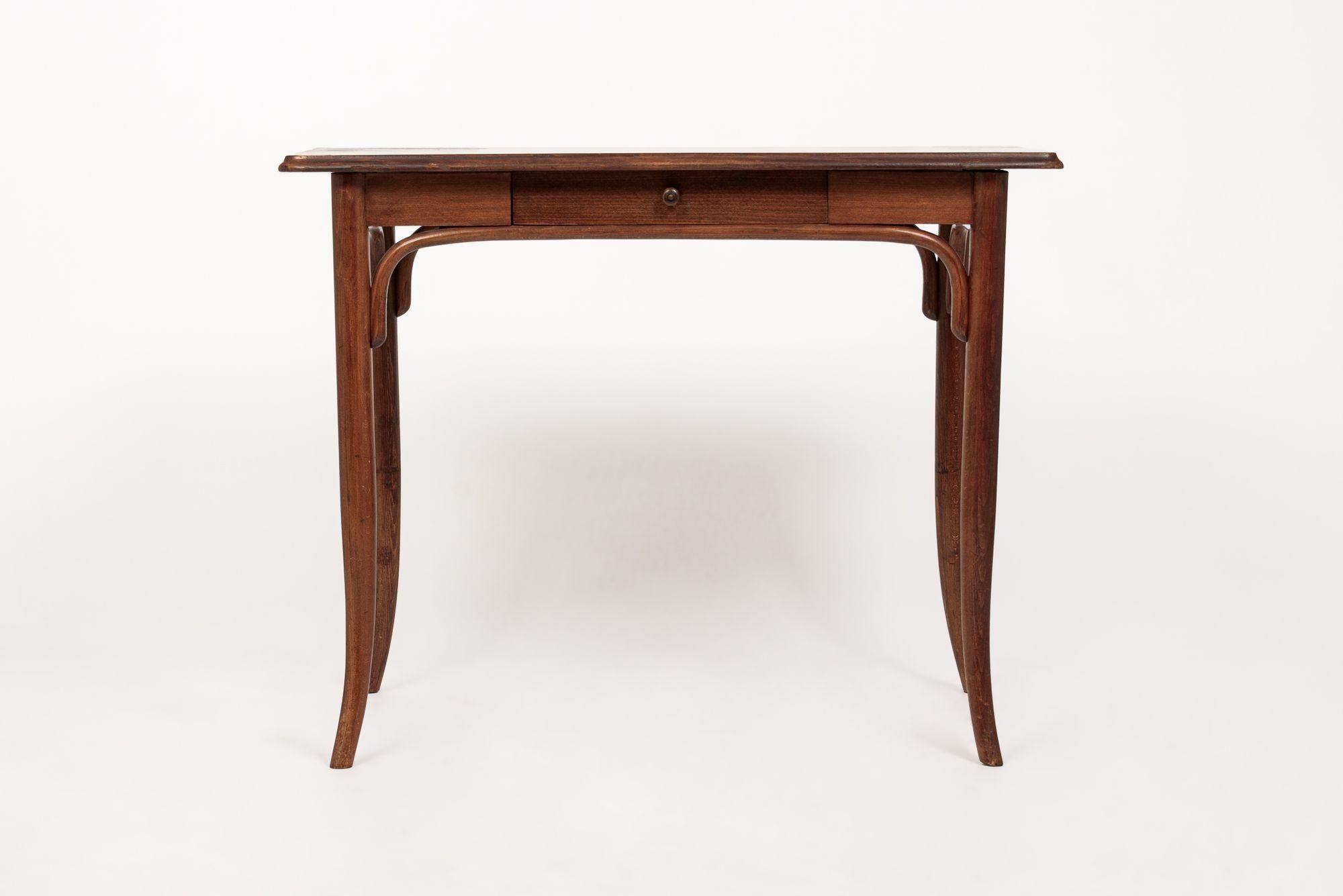 This lovely antique wooden writing desk table in the style of Thonet is circa 1920 and likely Austrian. This desk table has a beautiful proportion and simple elegance with clean lines and gentle curves and slender, tapered legs. The table is