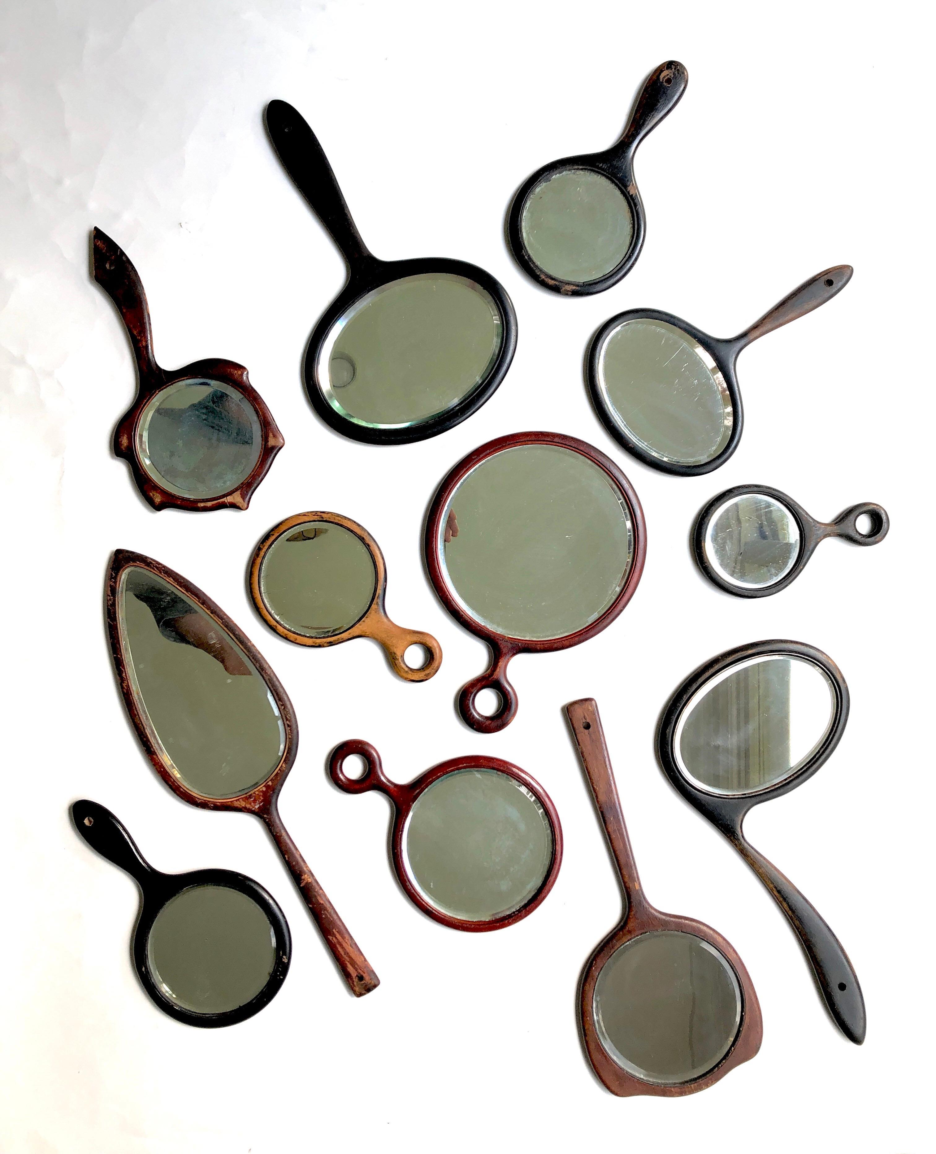 A collection of 12 antique beveled glass wooden hand mirrors in various shapes, colors and sizes. The ebony ones are most likely from England. Endless display possibilities. The smallest being 4.5