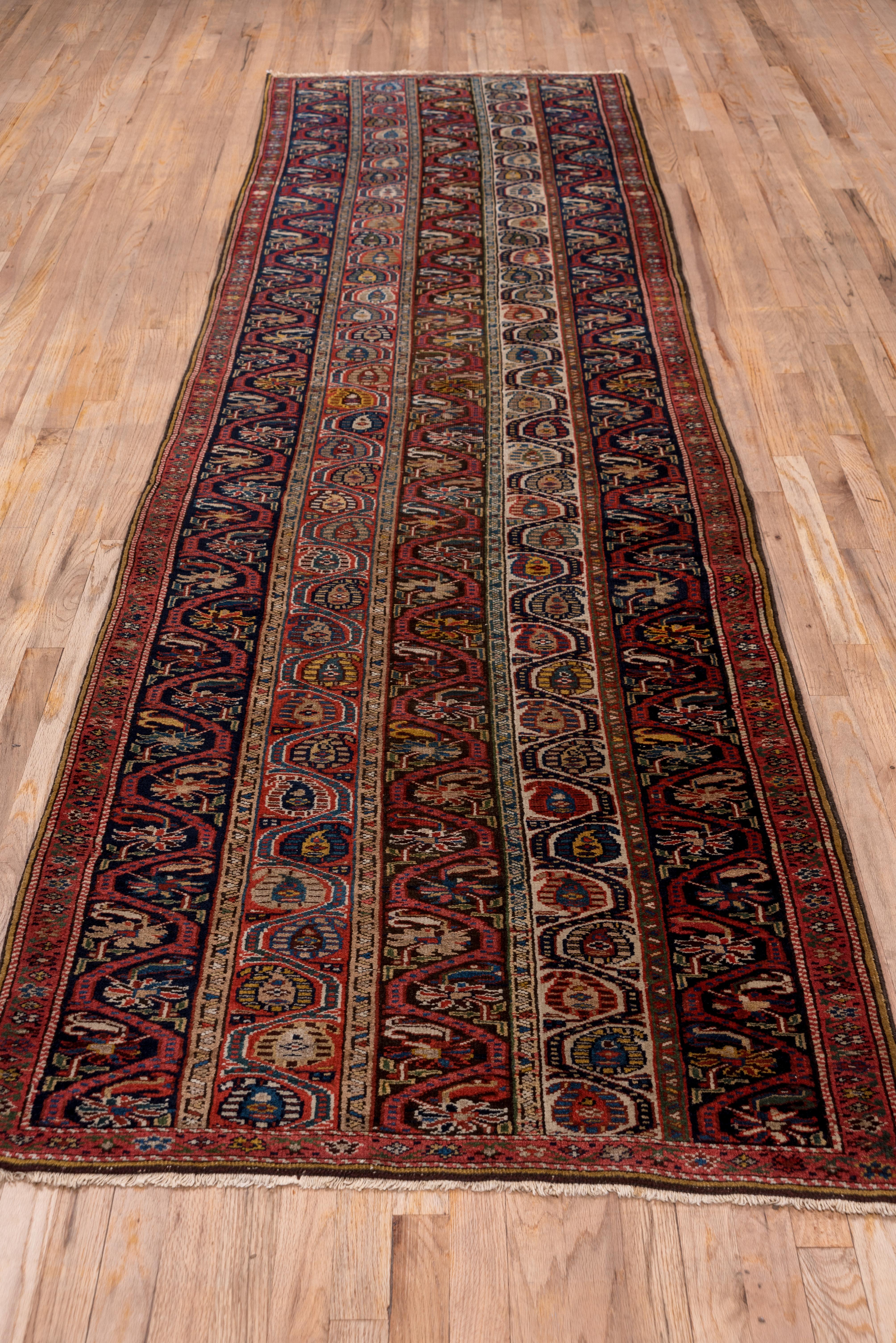 In the Caucasian style, this Kurdish Persian runner displays five columns strips in navy, red and ivory featuring bottehs and palmettes within undulating vines. The colors are rich and all natural, the weave is rock solid and board-like, and the