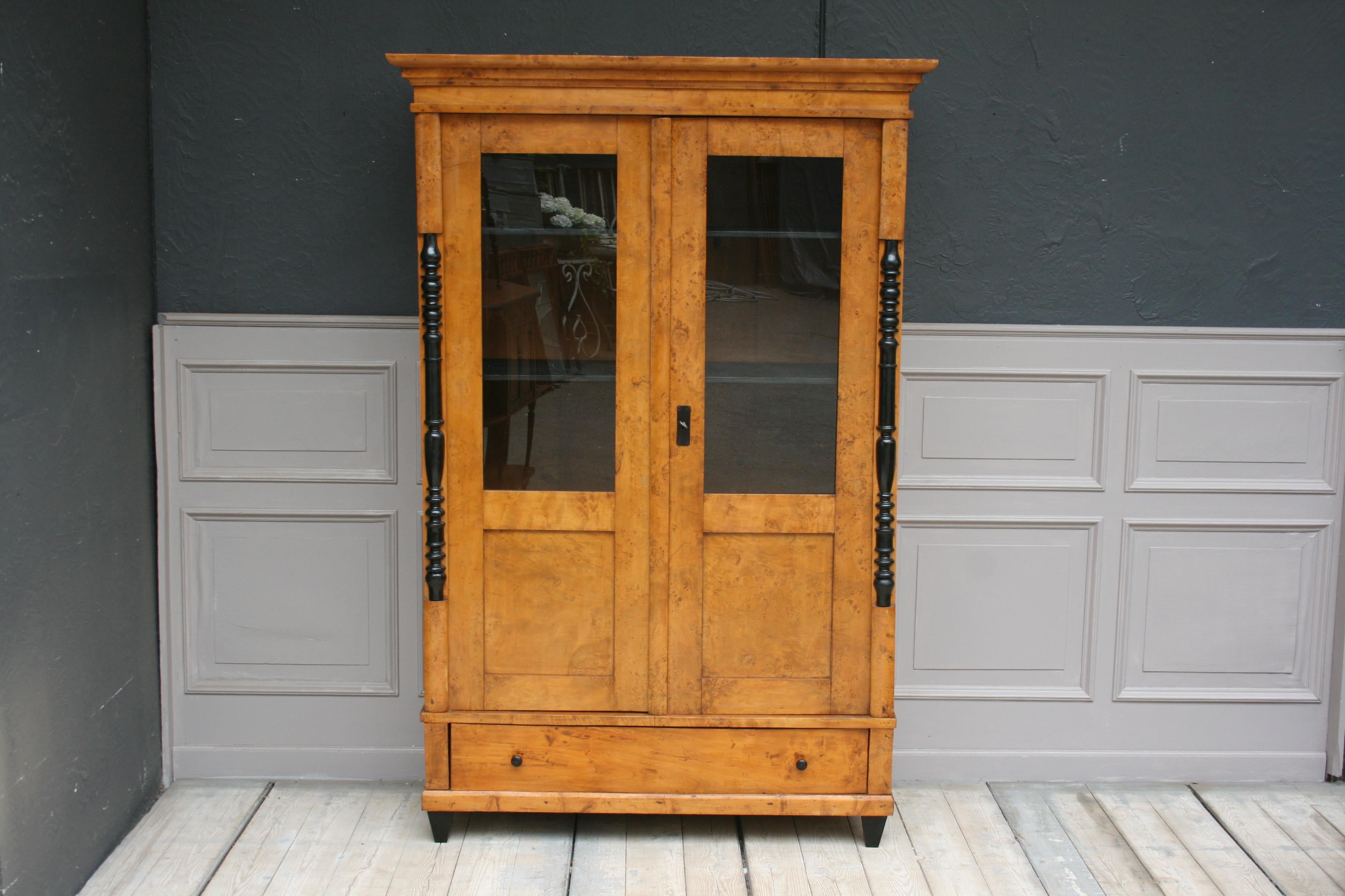 Rare German bird's eye maple Biedermeier showcase or bookcase from the 1st half of the 19th century. Solid maple and maple veneer on pine.

Two-door body with base drawer standing on four ebonized pointed feet. Pilaster strips decorated with