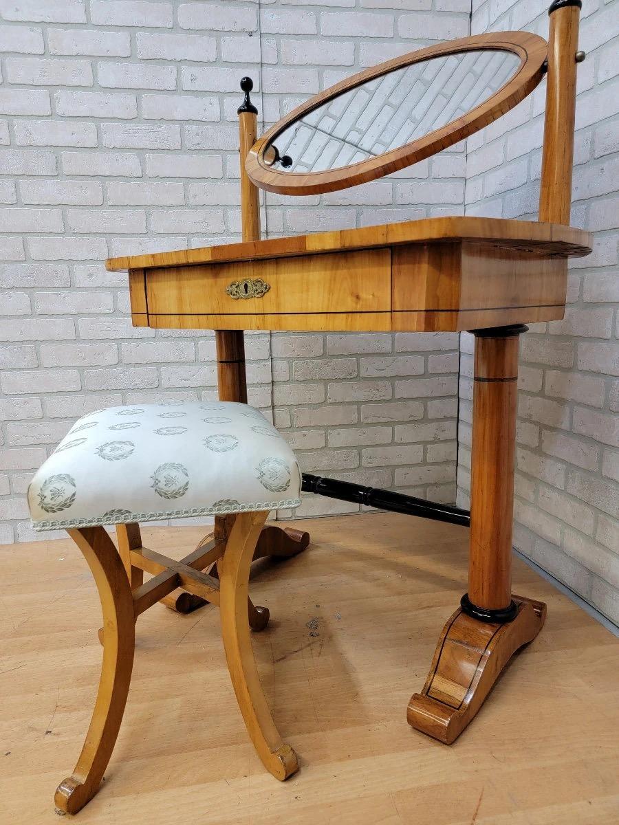 Table de coiffeuse et tabouret Biedermeier ovale en merisier antique - 2 pièces

Cette ancienne table de toilette Biedermeier comporte un tiroir et un miroir ovale à balancier avec un dossier tapissé de soie. Le miroir se balance sur deux poteaux