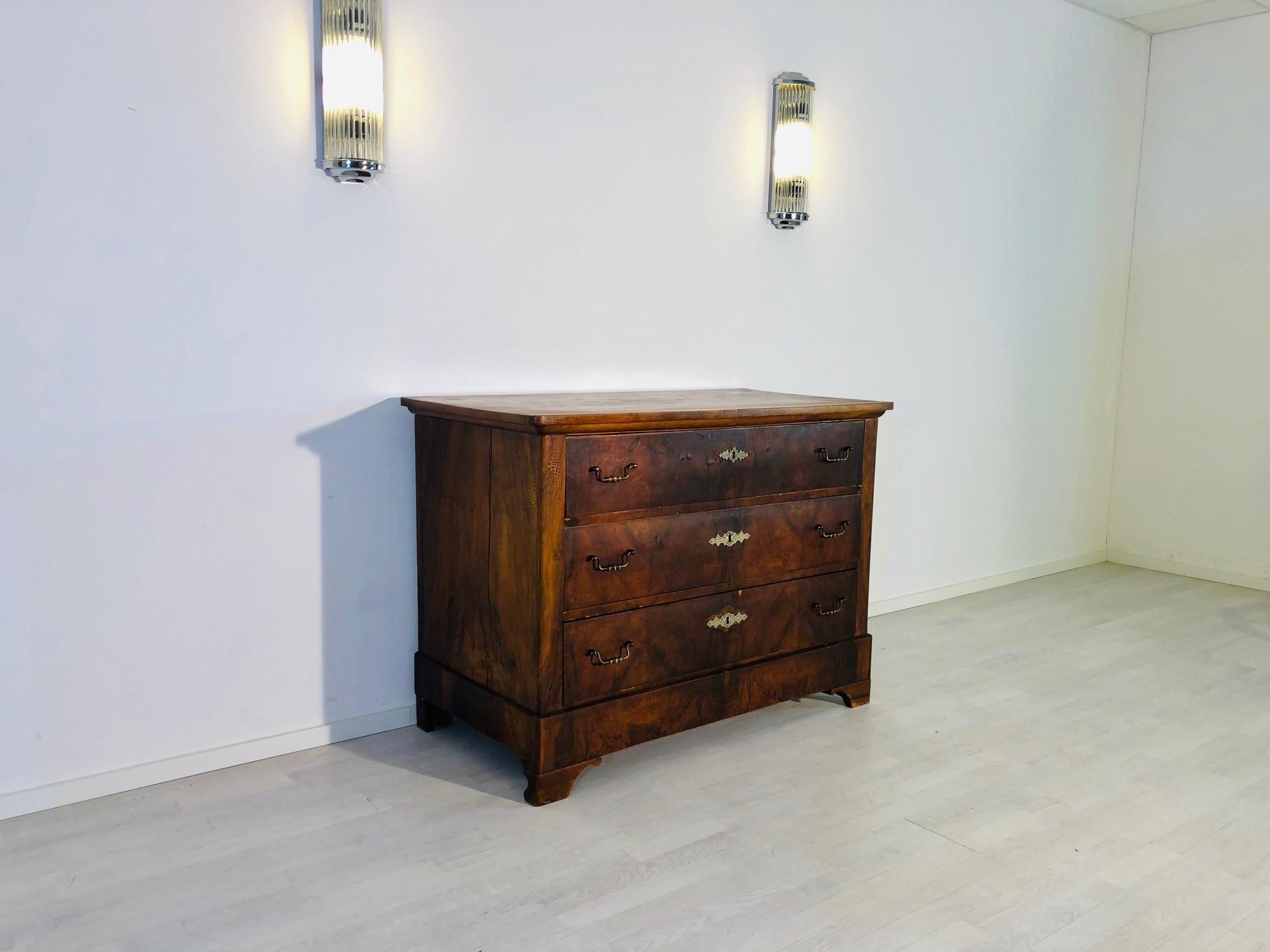 Original antique Biedermeier commode from a German castle, build in the 1850s. It convinces with its classic design, the dark brown walnut veneer and original key plates and handles made of brass. The item is currently under restoration and will be