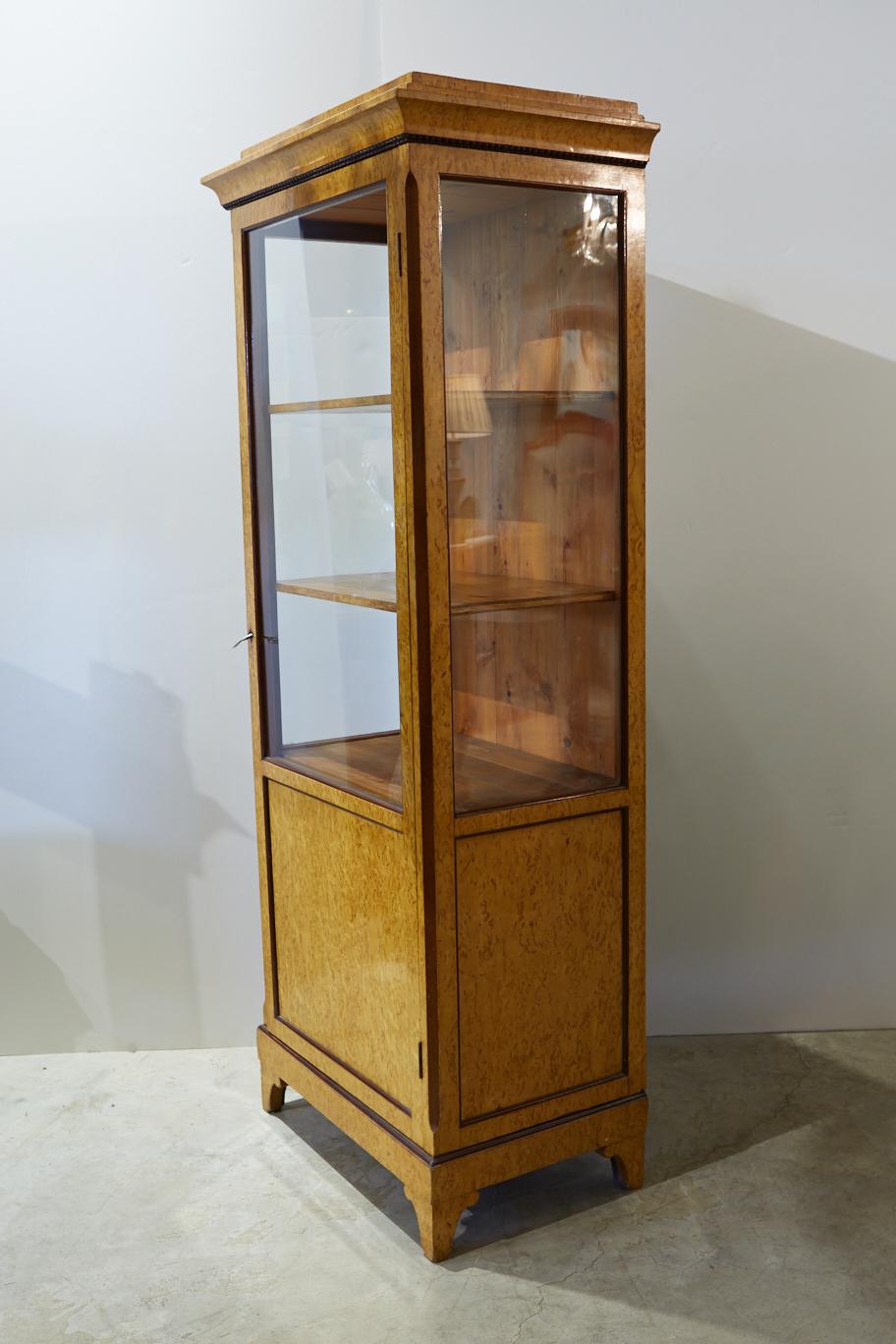 19th century Biedermeier display or curio cabinet in bird's-eye maple with brown lacquered molding trim. The door and one of the side panels appear to be antique glass; one of the side panels might be a replacement. The interior of the cabinet and