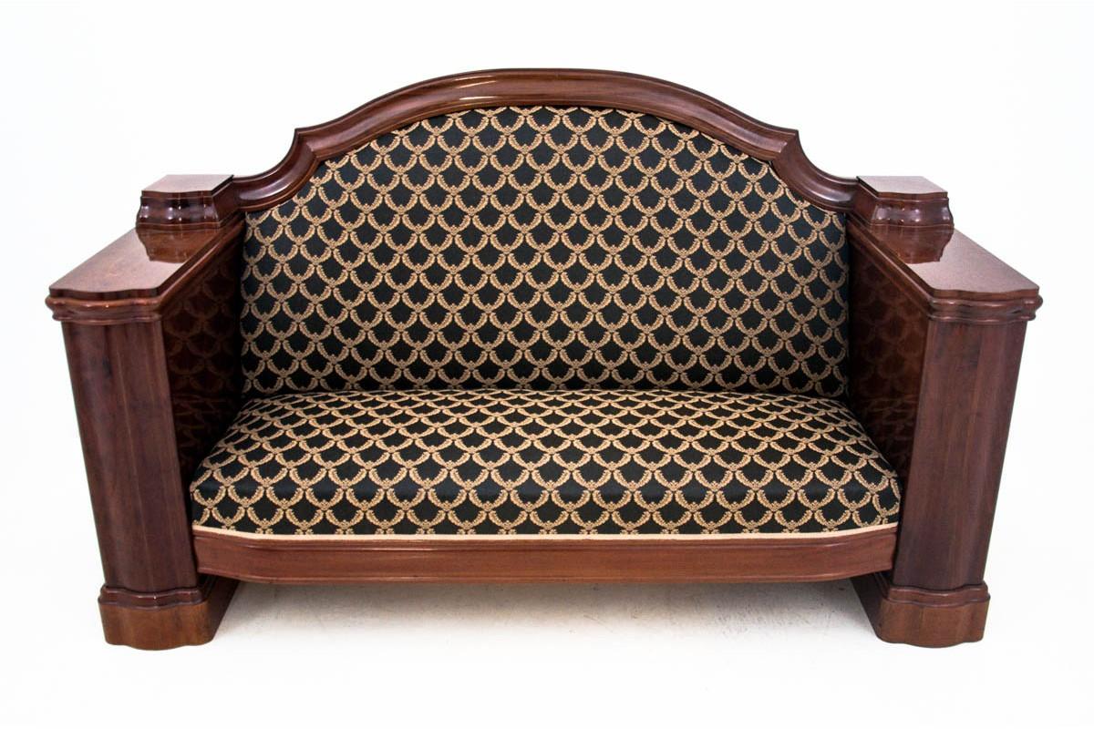The mahogany sofa was made in the mid-19th century in the Biedermeier style. A couch with a classic stile profile, upholstered with fabric on the seat and backrest. Monumental wooden armrests give the sofa a refined character. A great choice for a