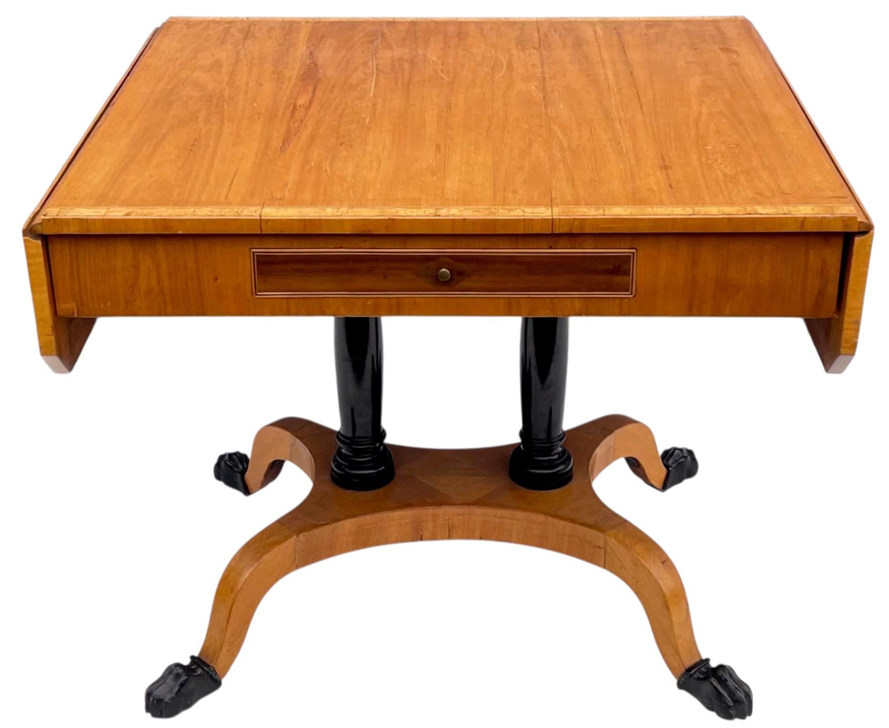 Se trata de una antigua mesa de trabajo de hoja abatible de estilo Biedermeier continental. La parte superior está listada con madera de satén. Los pedestales y las patas comieron Ebonizado. La pieza tiene un único cajón de cola de milano. ¡Es un