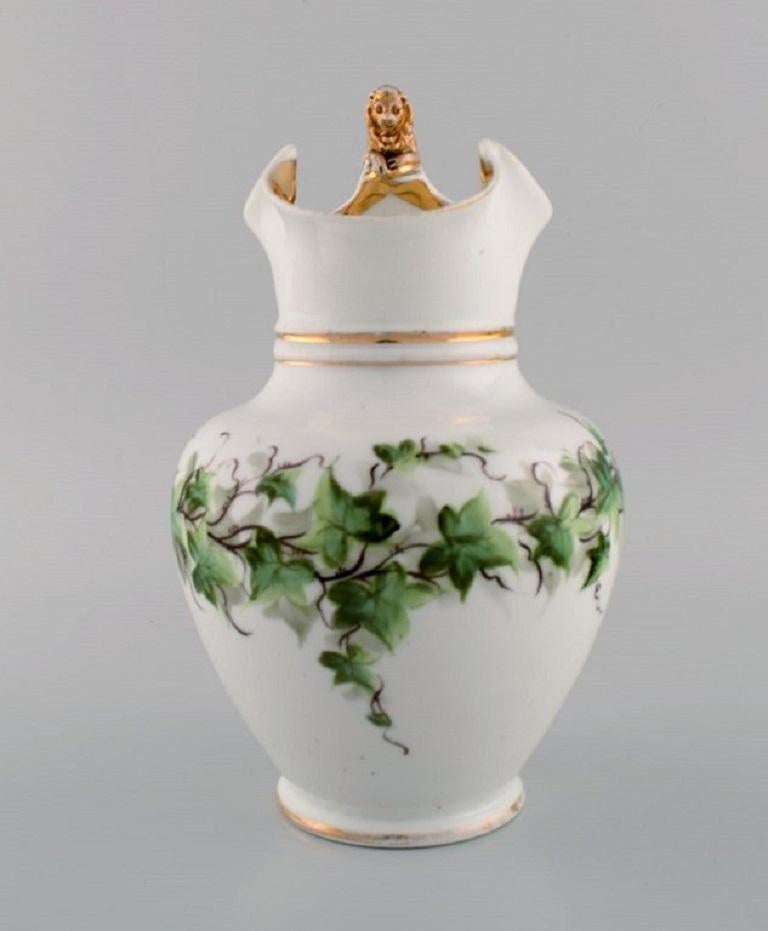 Ancienne carafe à chocolat Bing & Grøndahl en porcelaine avec un lion sur l'anse. 
Fleurs peintes à la main et décoration dorée. 1870s.
Mesures : 24.5 x 17 cm.
En bon état d'origine. Usure normale sans éclats ni fissures.
Estampillé.