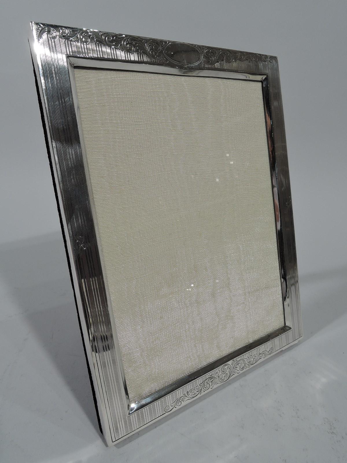 Edwardian sterling silver picture frame. Made by Birks in Montreal. Rectangular window and flat surround with bevelled interior rim. Vertical pinstripes and foliate scrolls on top and bottom rails. Oval frame (vacant). For vertical (portrait)
