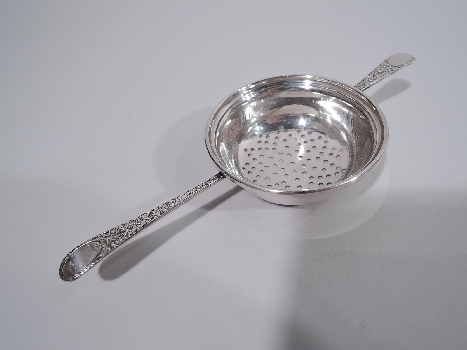 Edwardian sterling silver tea strainer. Made by Birks in Canada, ca 1920. Round bowl with pierced-star bottom. Tapering handle mounted to one side; shorter same mounted to other. Supports have pretty scrollwork and oval terminals (vacant). Majorly