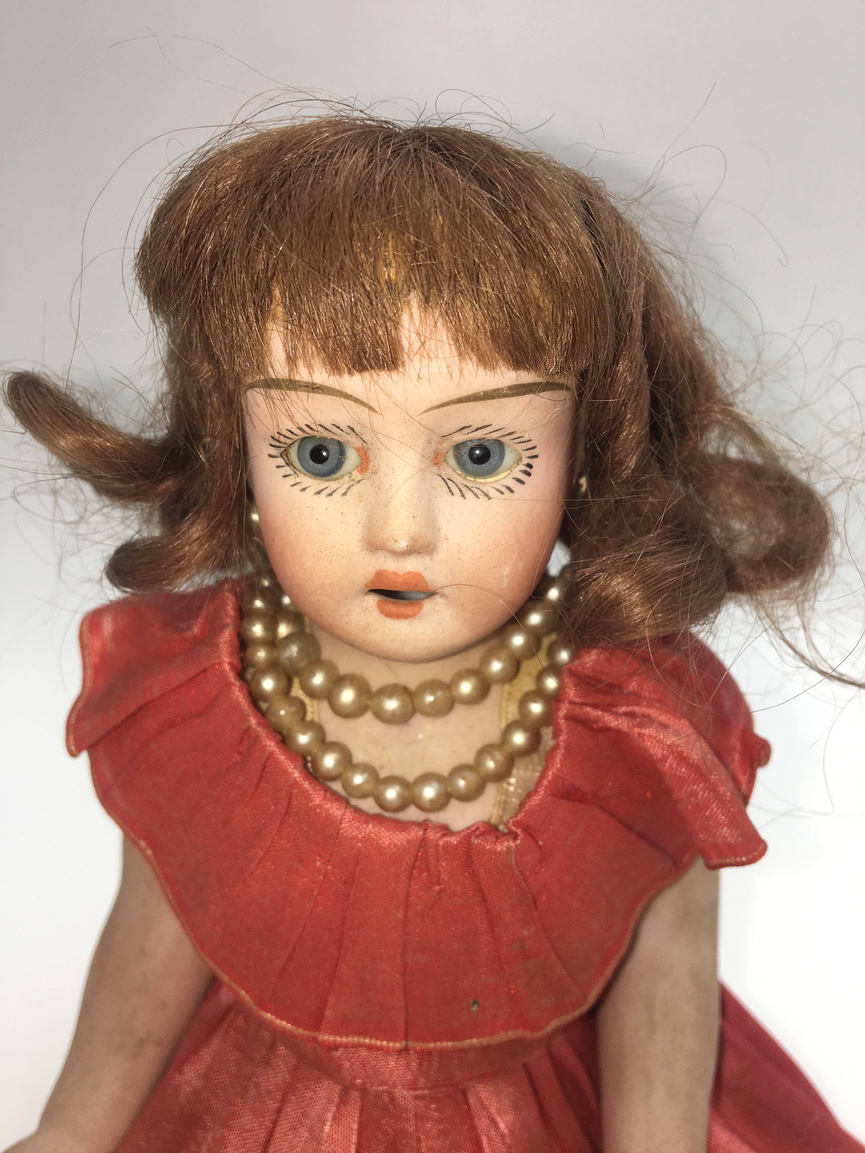 Old Bisque ceramic doll of the twentieth century.
Short dress in red fabric with champagne lace petticoat, necklace in period style.